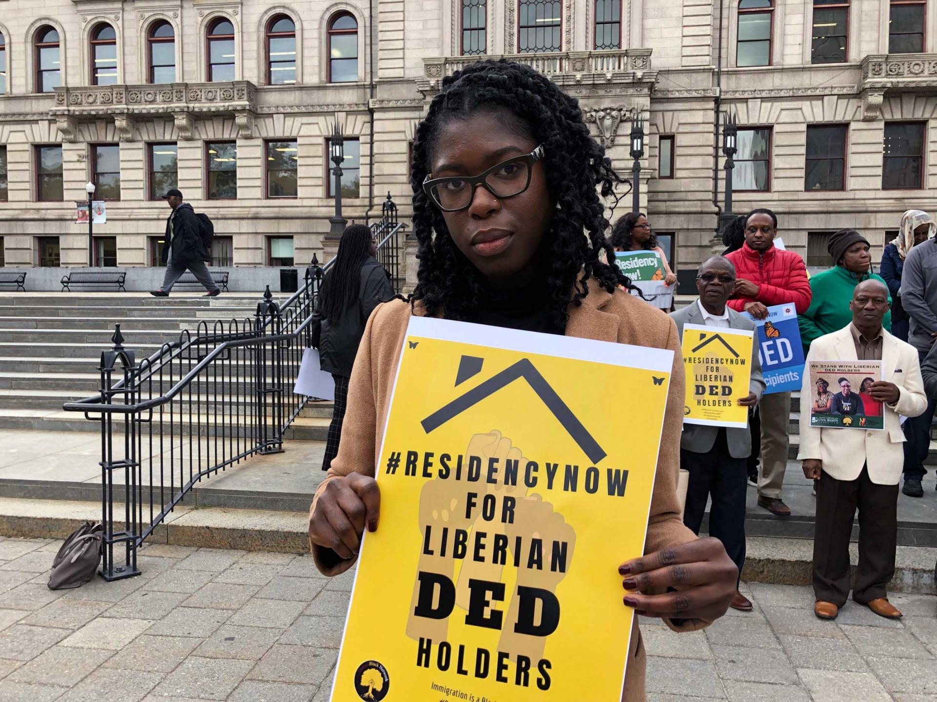 A woman holds a sign that reads, "Residency now for Liberian DED holders." 