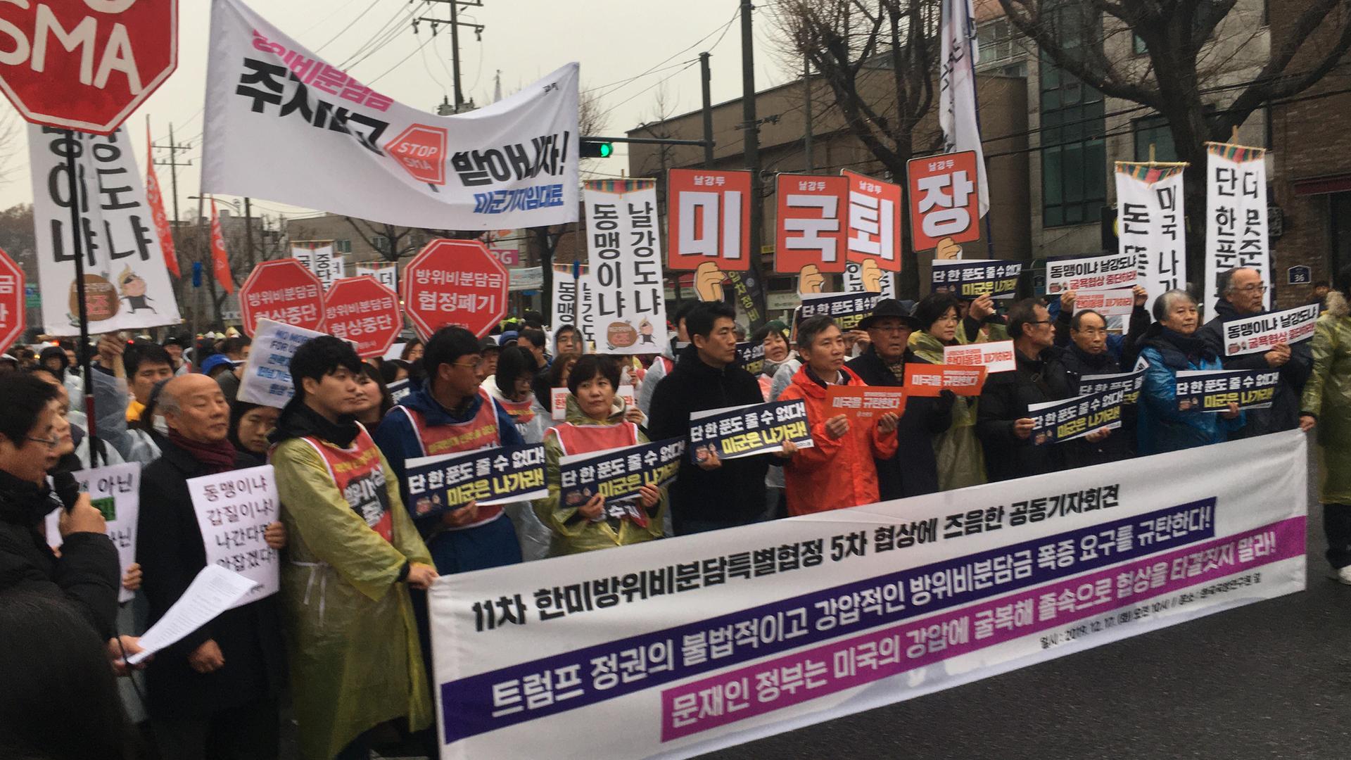 A group of protesters march with a large banner with large words in Korean language