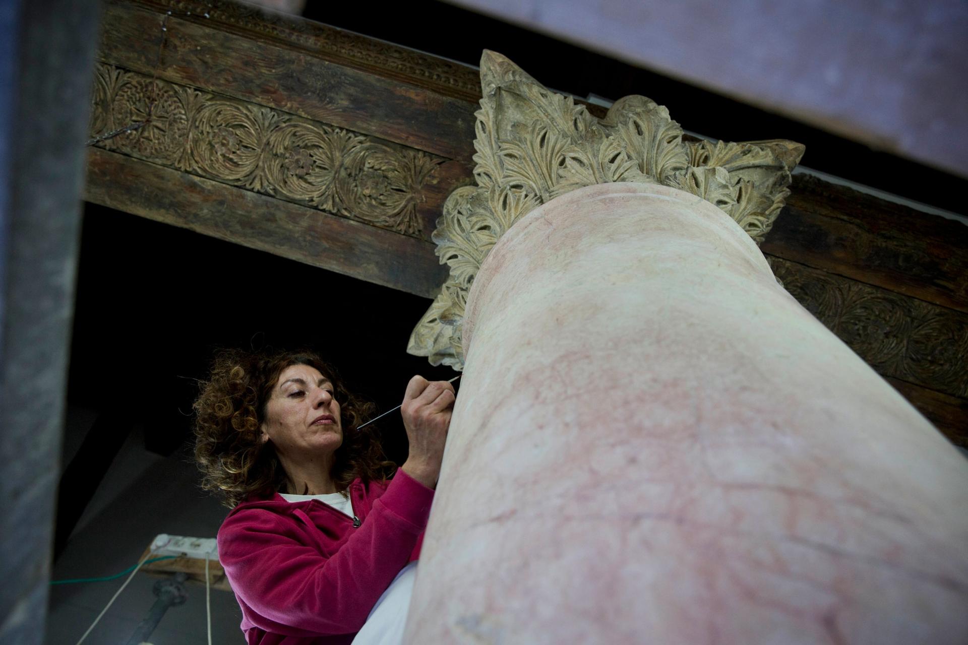 A woman is shown wearing a purple sweater and holding a small brush performing restoration on a granite column.