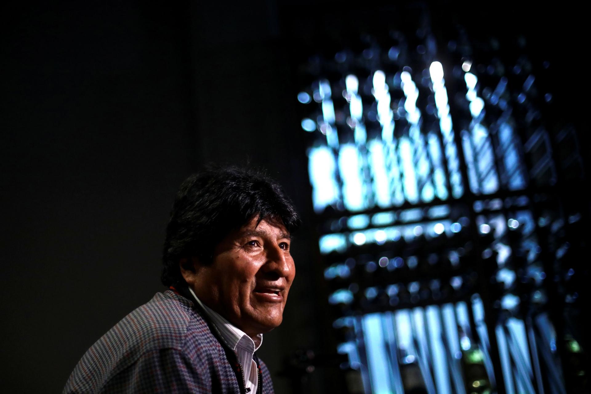 Former Bolivian President Evo Morales is shown wearing a jacket with light streaming through a window in the distance.