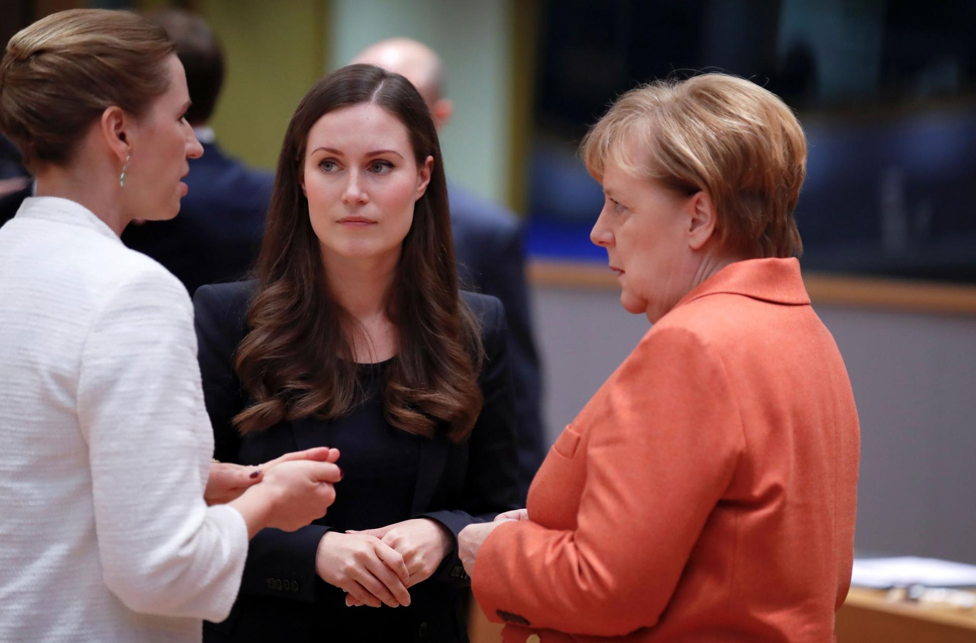 German Chancellor Angela Merkel, Finland's Prime Minister Sanna Marin and Denmark's Prime Minister Mette Frederiksen are shown standing, facing each other and talking.