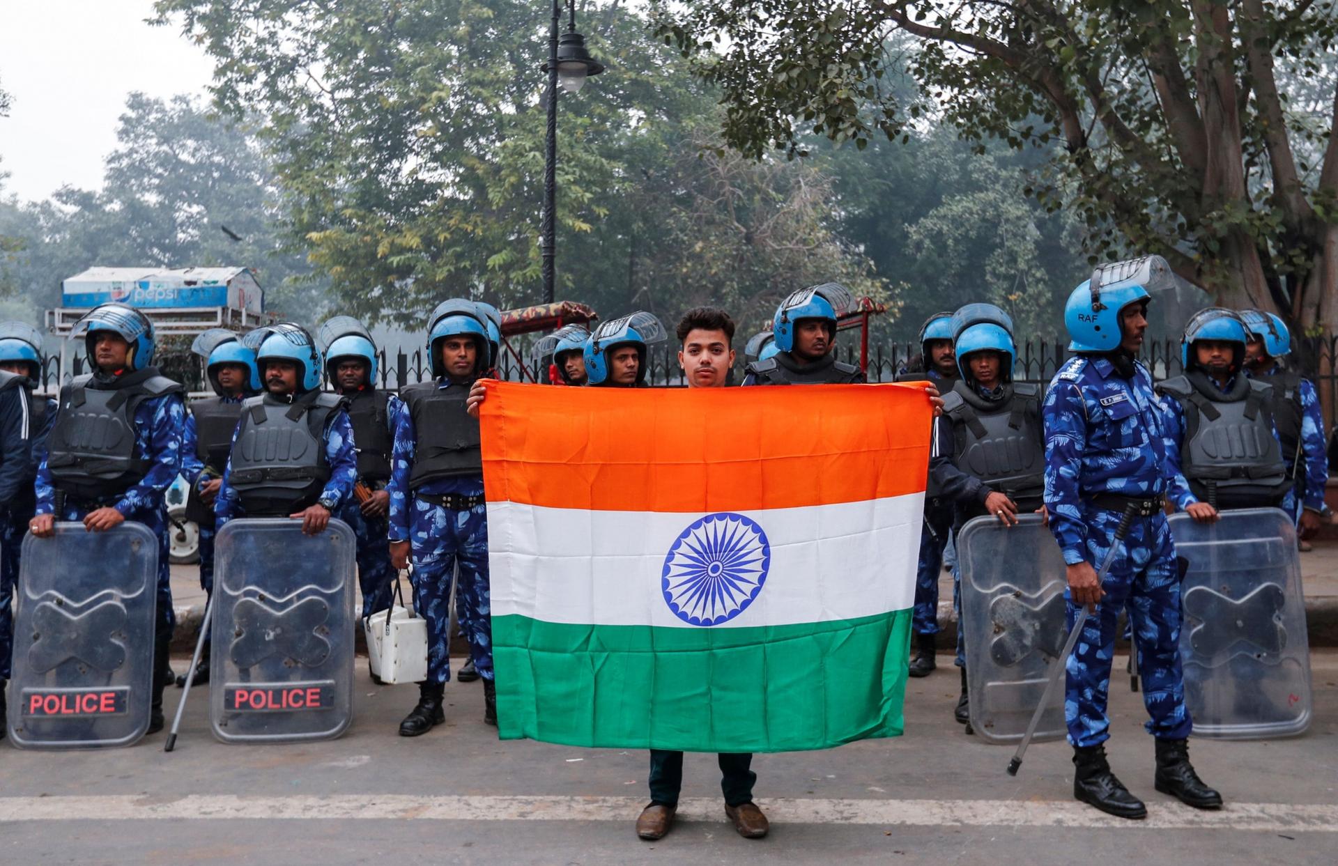 A man holds Indian flag in front of police wearing blue uniforms. 