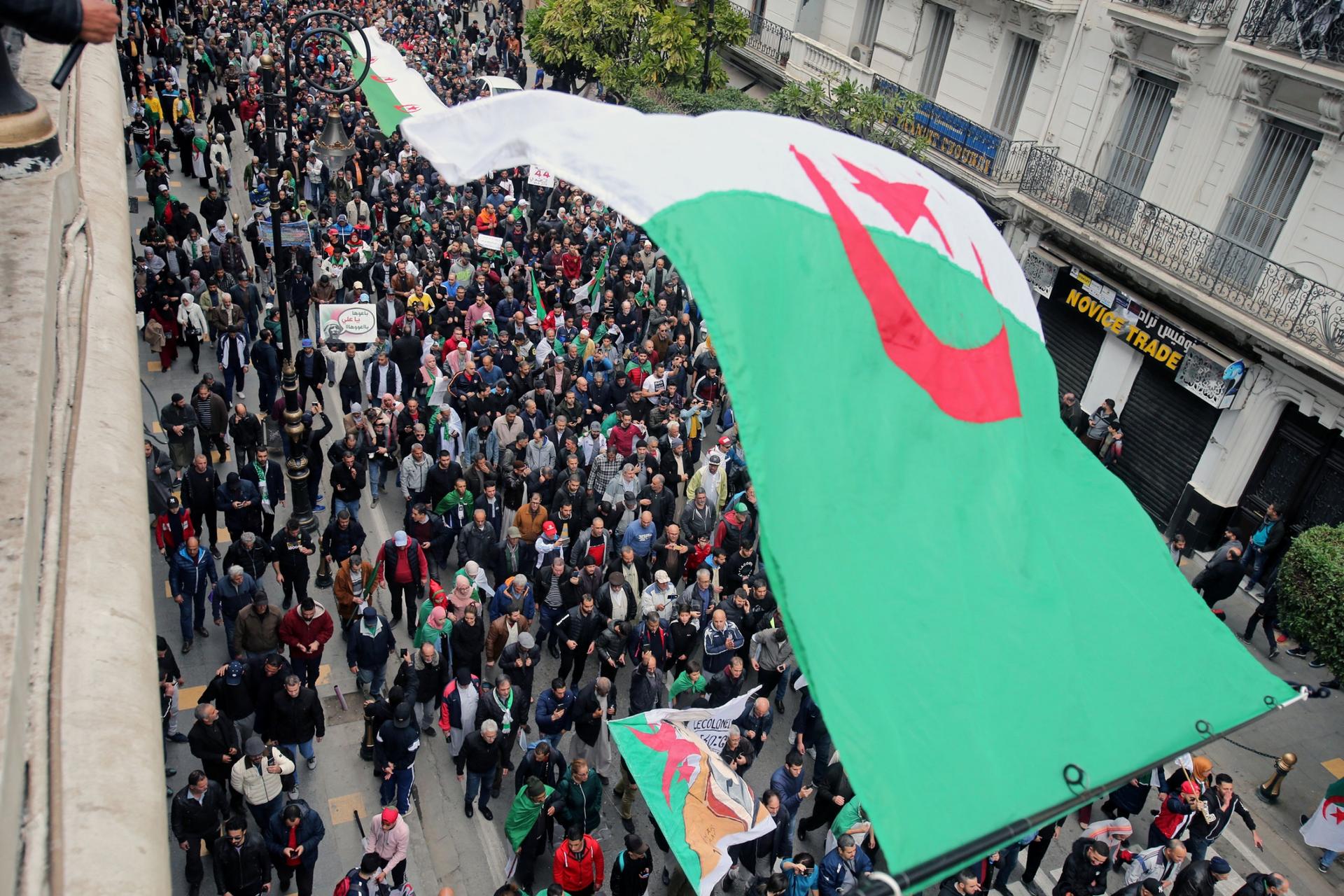 A street is shown filled with people and an Algerian flag is in the nearground.