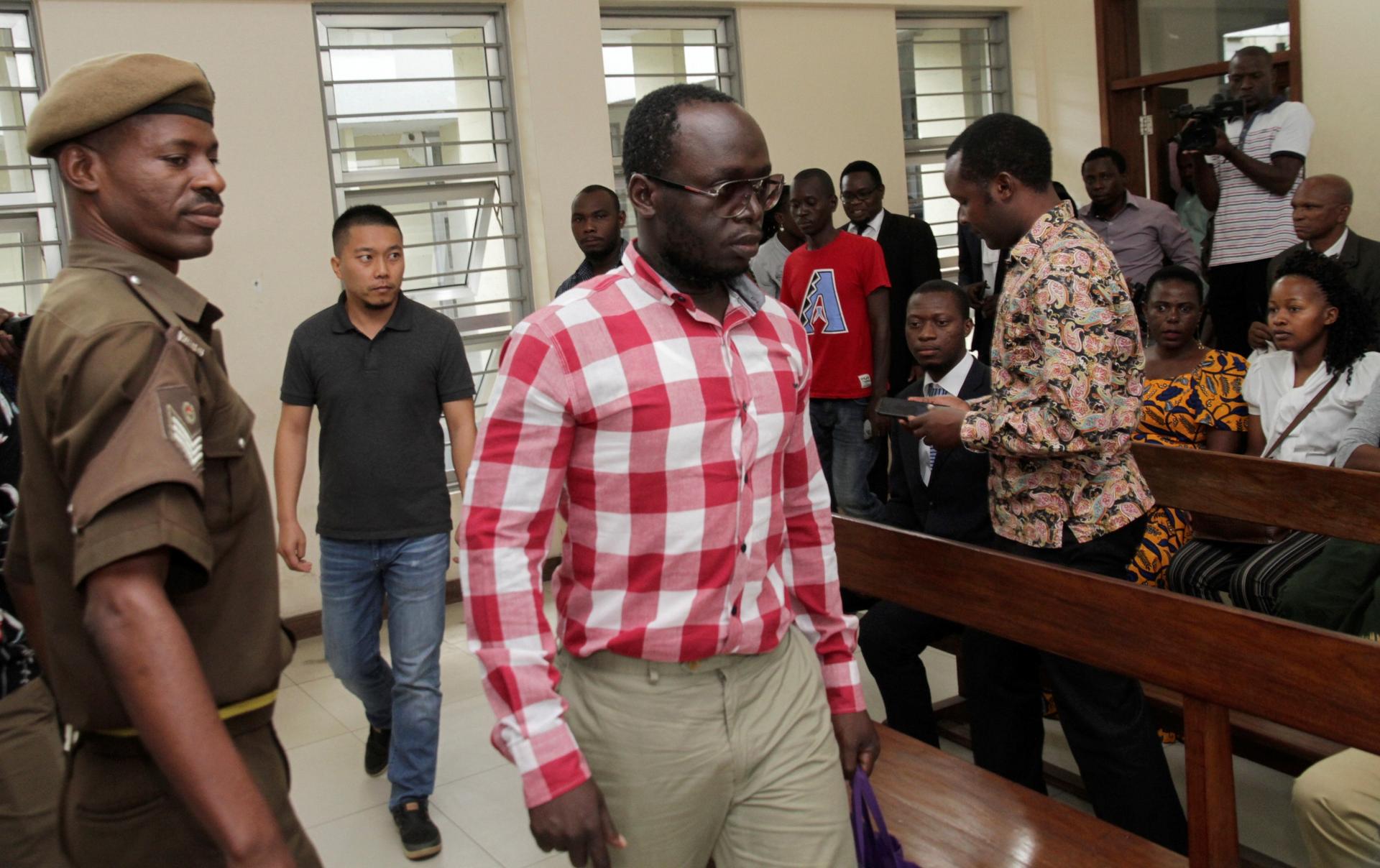 Erick Kabendera wears a white and red shirt and leaves a court room flanked by police