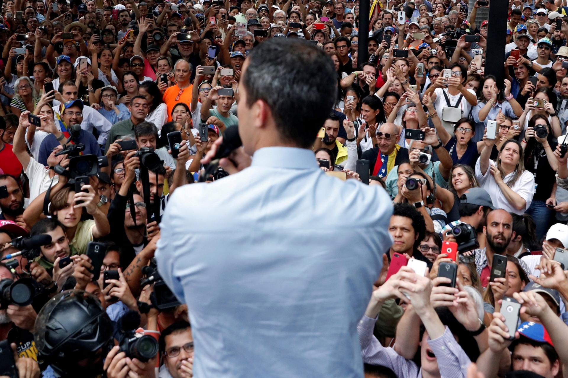 Venezuelan opposition leader Juan Guaidó is shown from behind while looking out on a large crowd.