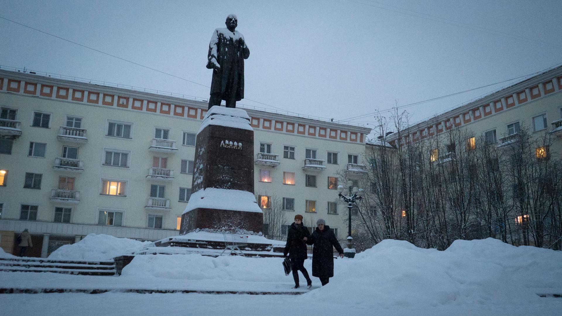 People walk past a snow covered statue of Soviet leader Vladimir Lenin.
