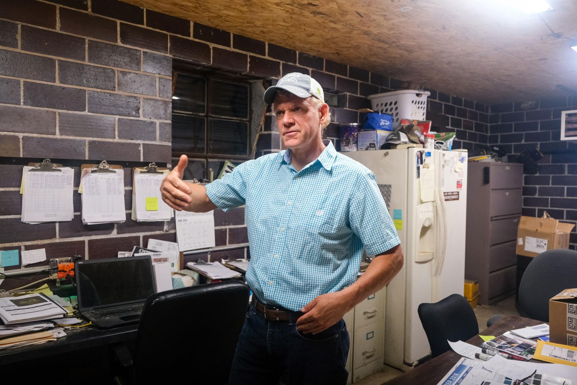 Corn and soybean farmer Bruce Peterson is shown standing in an office wearing a blue shirt and a gray hat.
