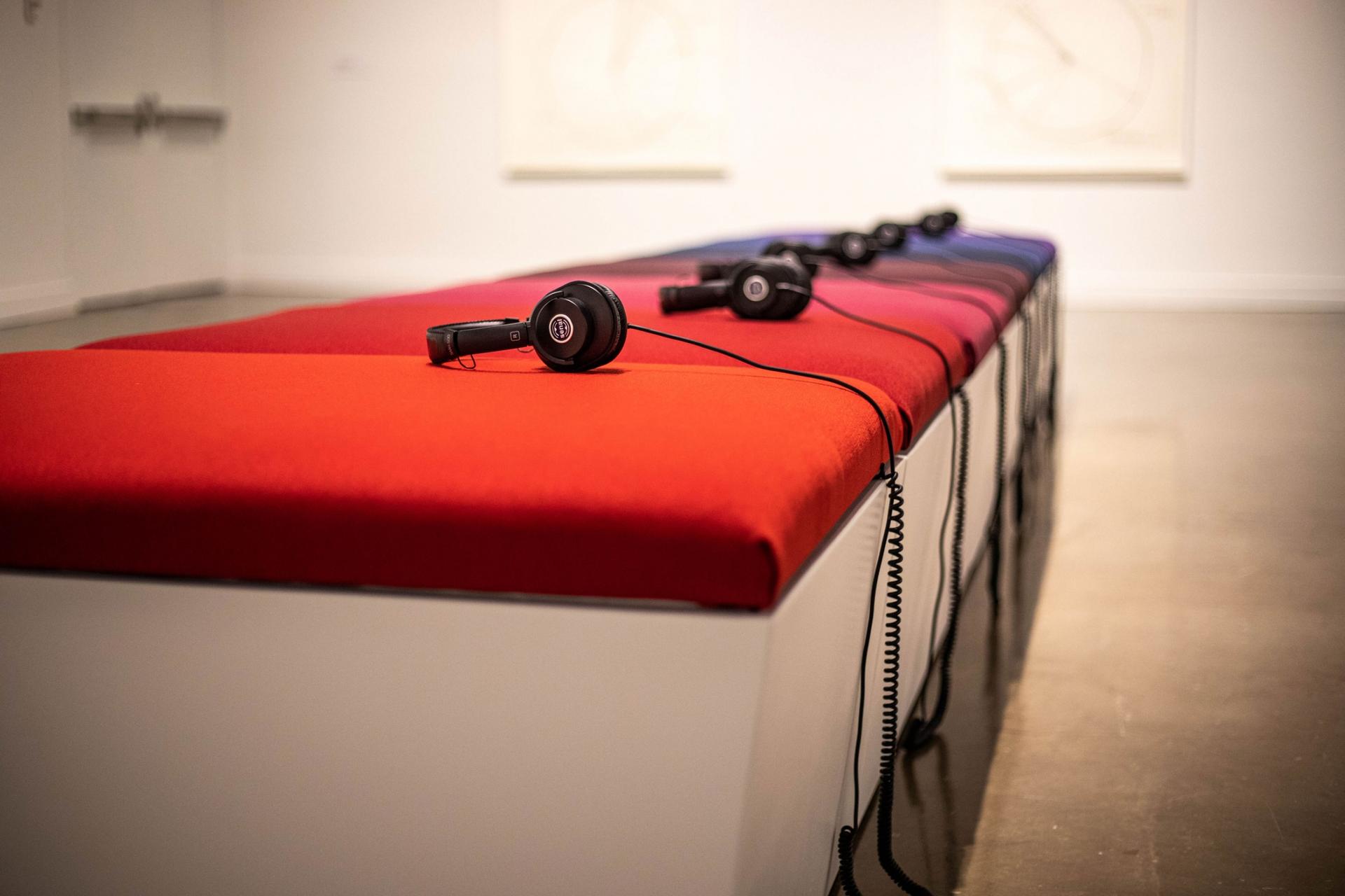 A long bench is shown with brightly colored cushions and headphones on each cushion.