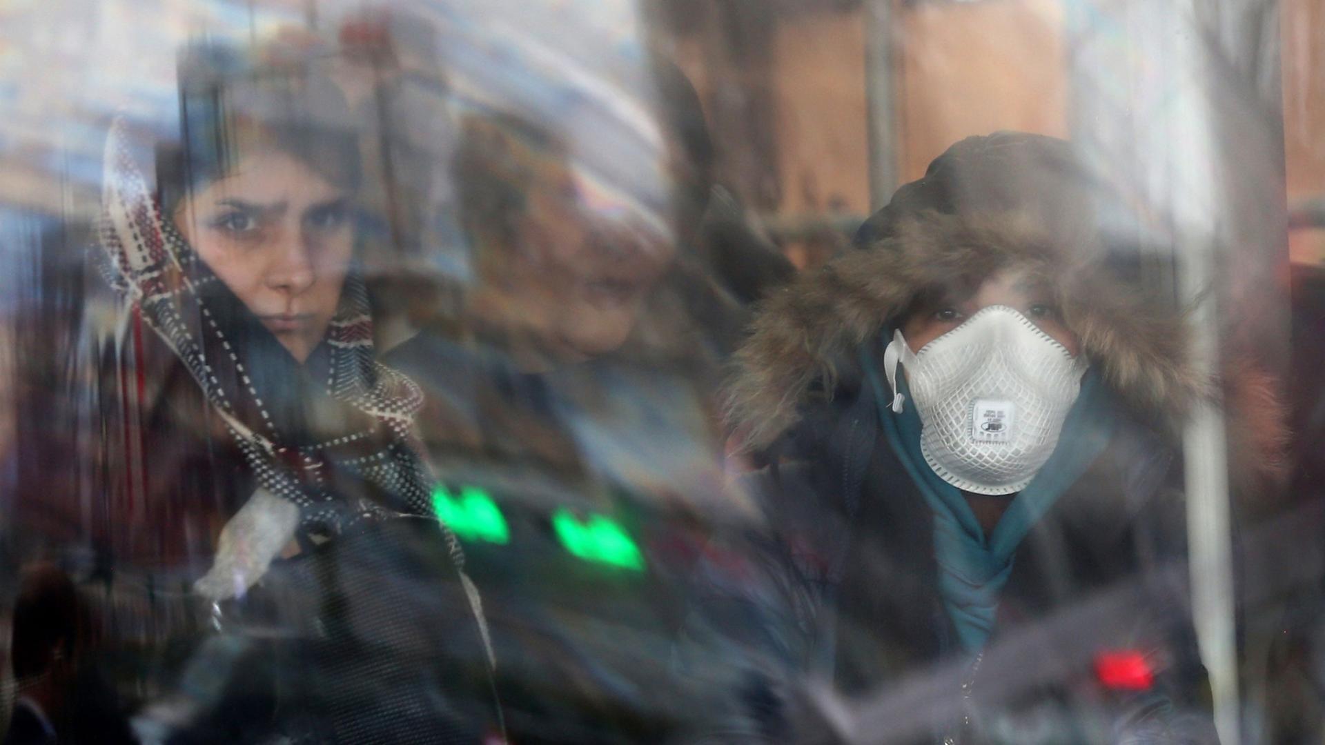 Women are shown through reflecting glass with one wearing a face mask and a hooded jacket.