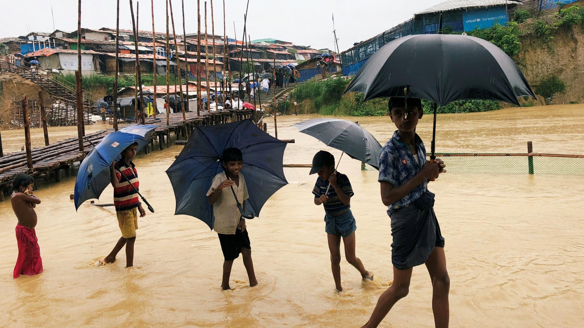 Young people walk through flood waters at refugee camp