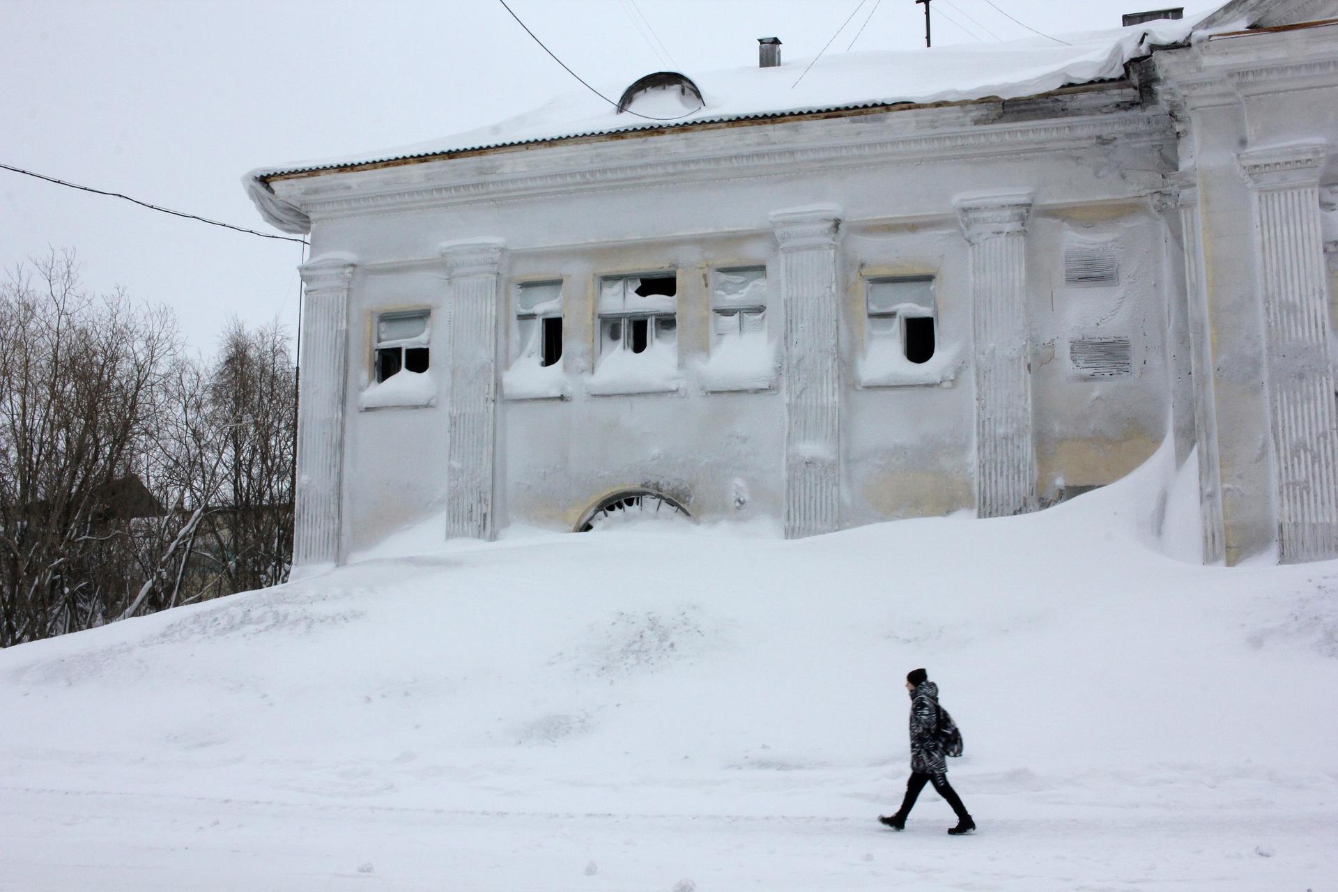 A man walks past an abandoned building in the snow