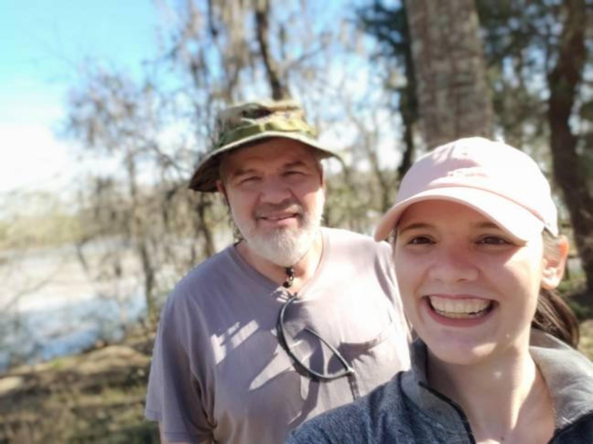 A photograph of Ashley Lucier who is wearing a pink hat and and her father, Anthony, who is standing behind her.