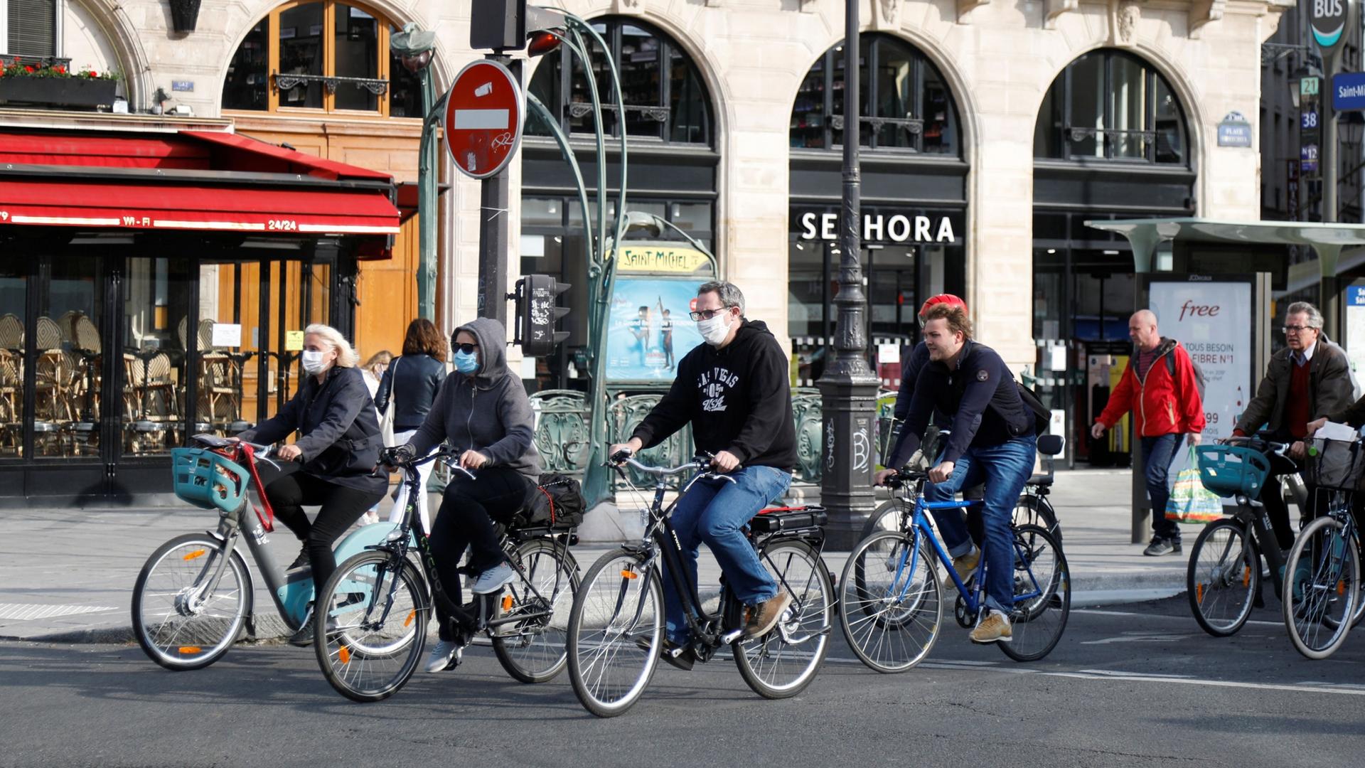 A group of several people are shown riding bicycles in the streets and wearing protective face masks.