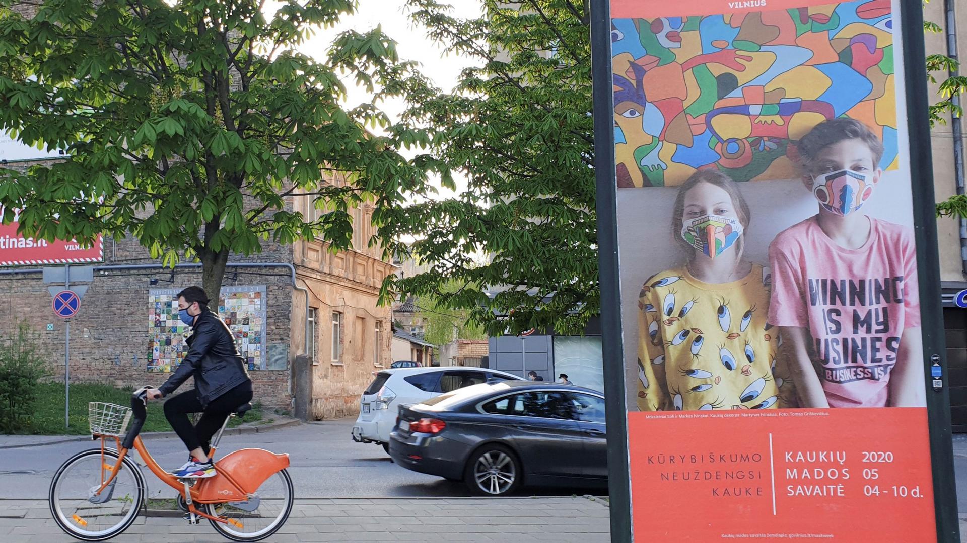 A person on an orange bicycle rides past a billboard of people with masks