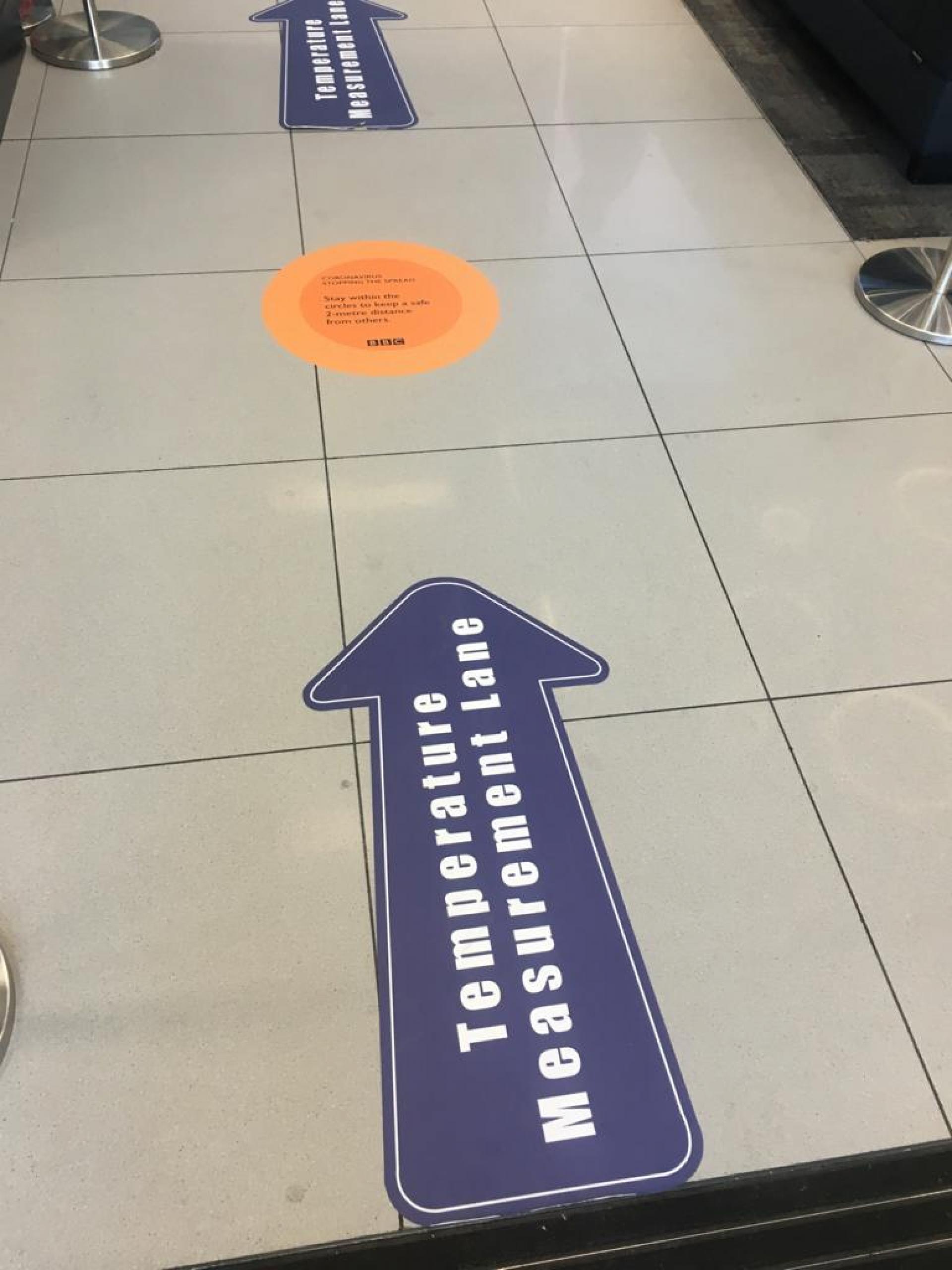 Signs on the floor at the BBC direct people to the thermal scanners. 