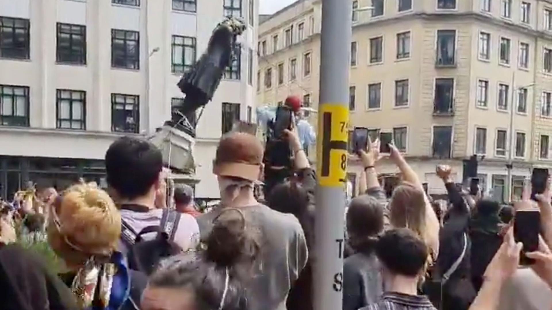 A large group of protesters are shown pulling down the metal statue of Edward Colston.