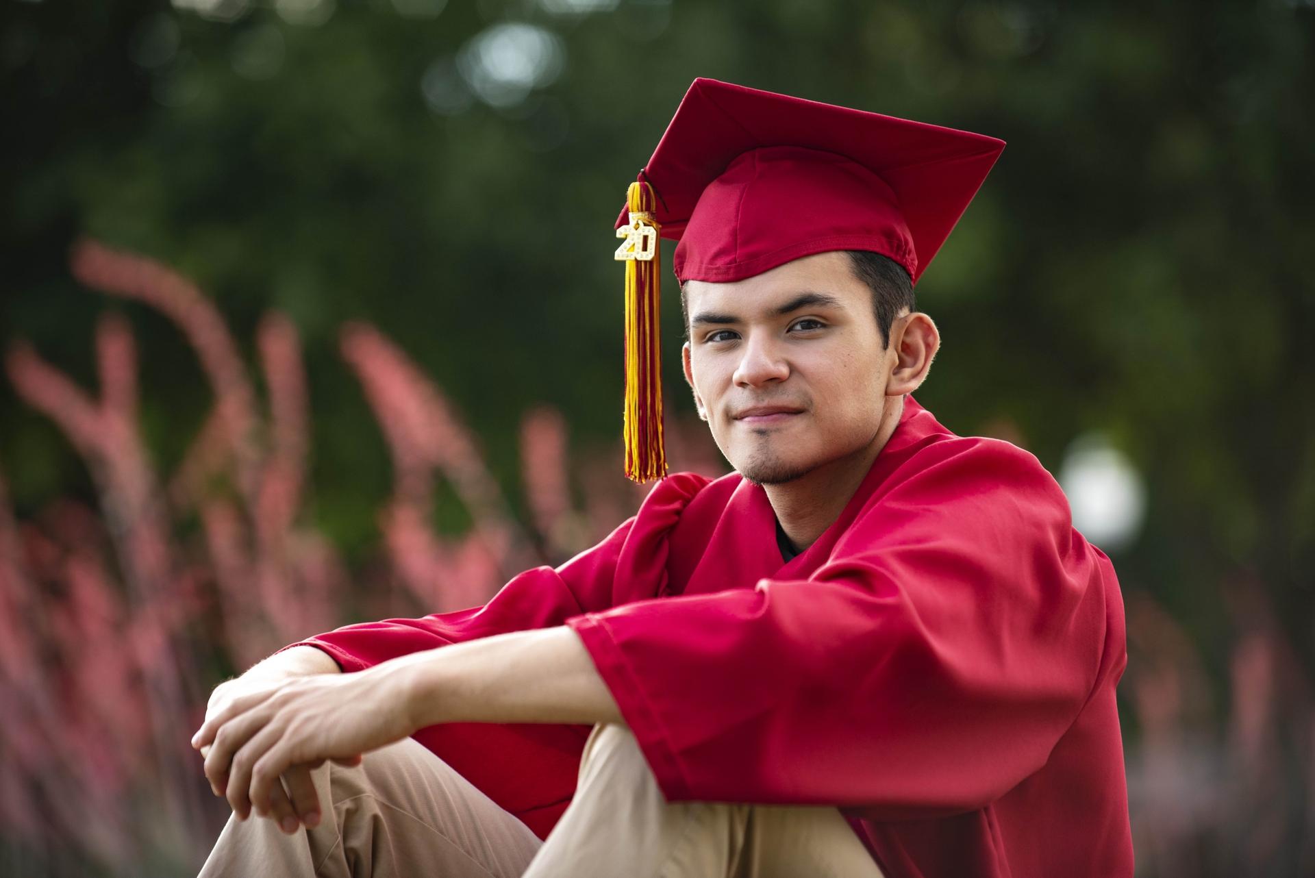 A young man wears a red graduation gown, cap and tassel.