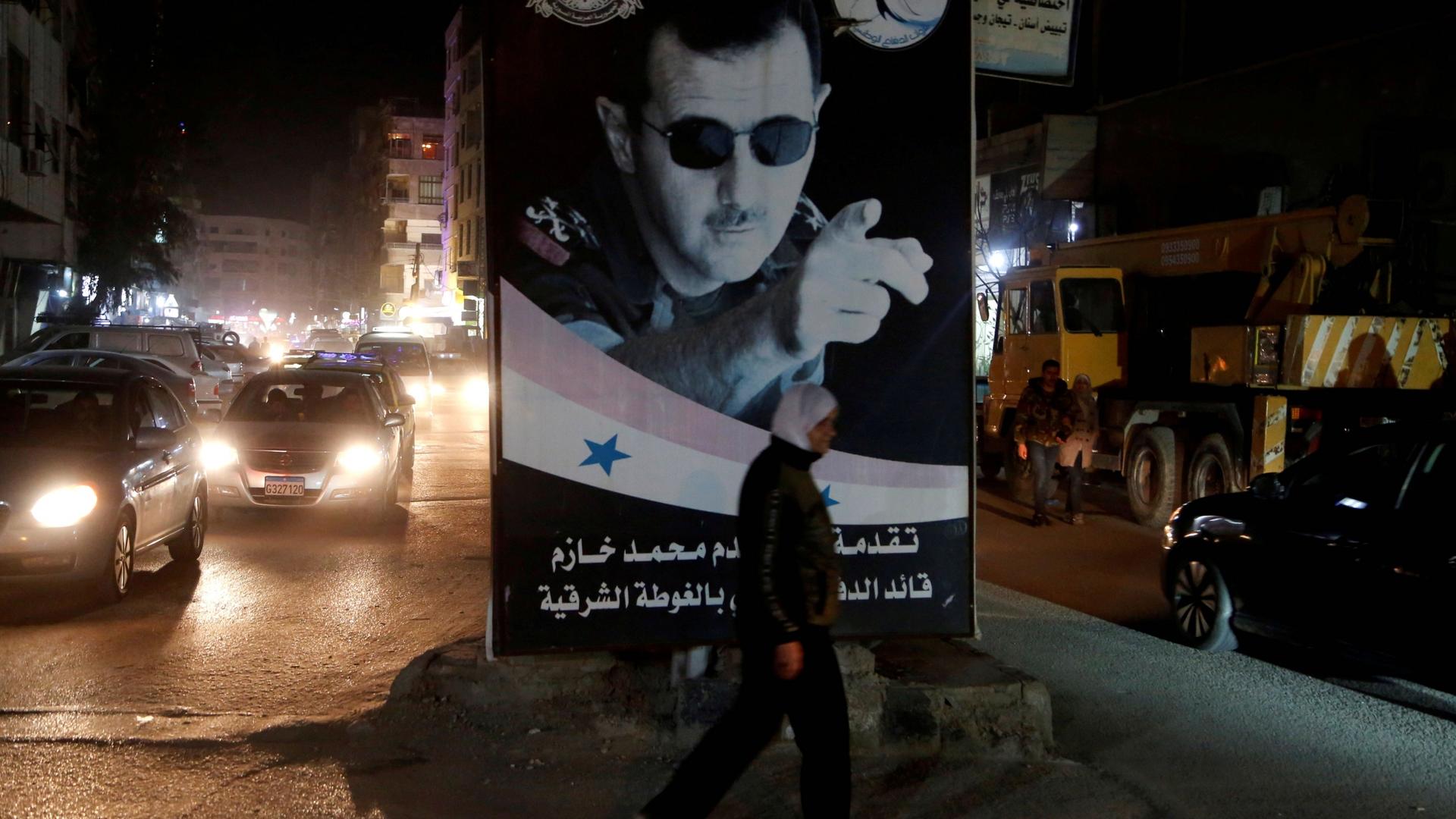 A woman walks past a poster depicting Syria's President Bashar al-Assad in Damascus, Syria, March 5, 2020. 