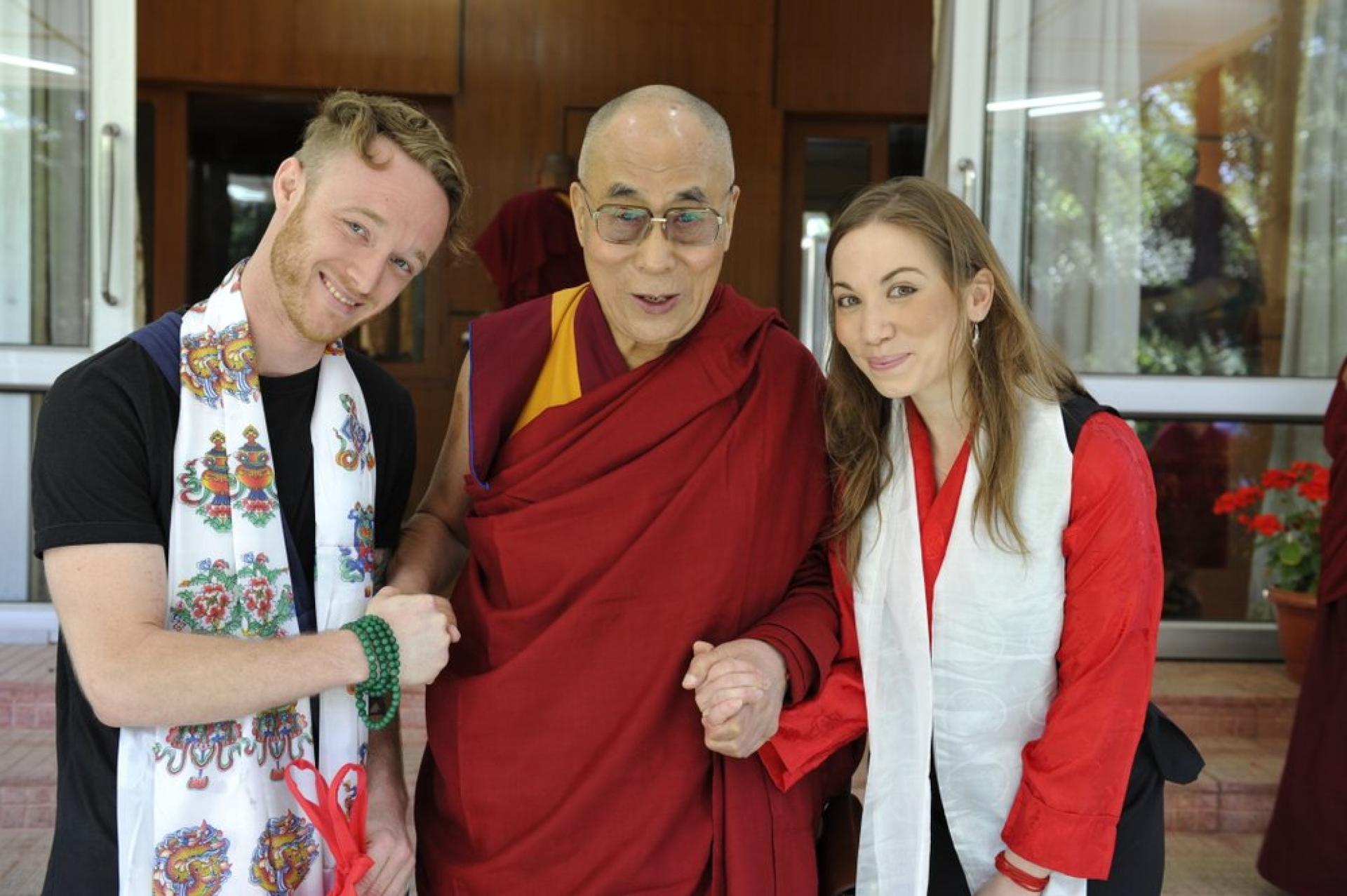 The Dalai Lama posses for a photo with a man and a woman. They are holding hands.