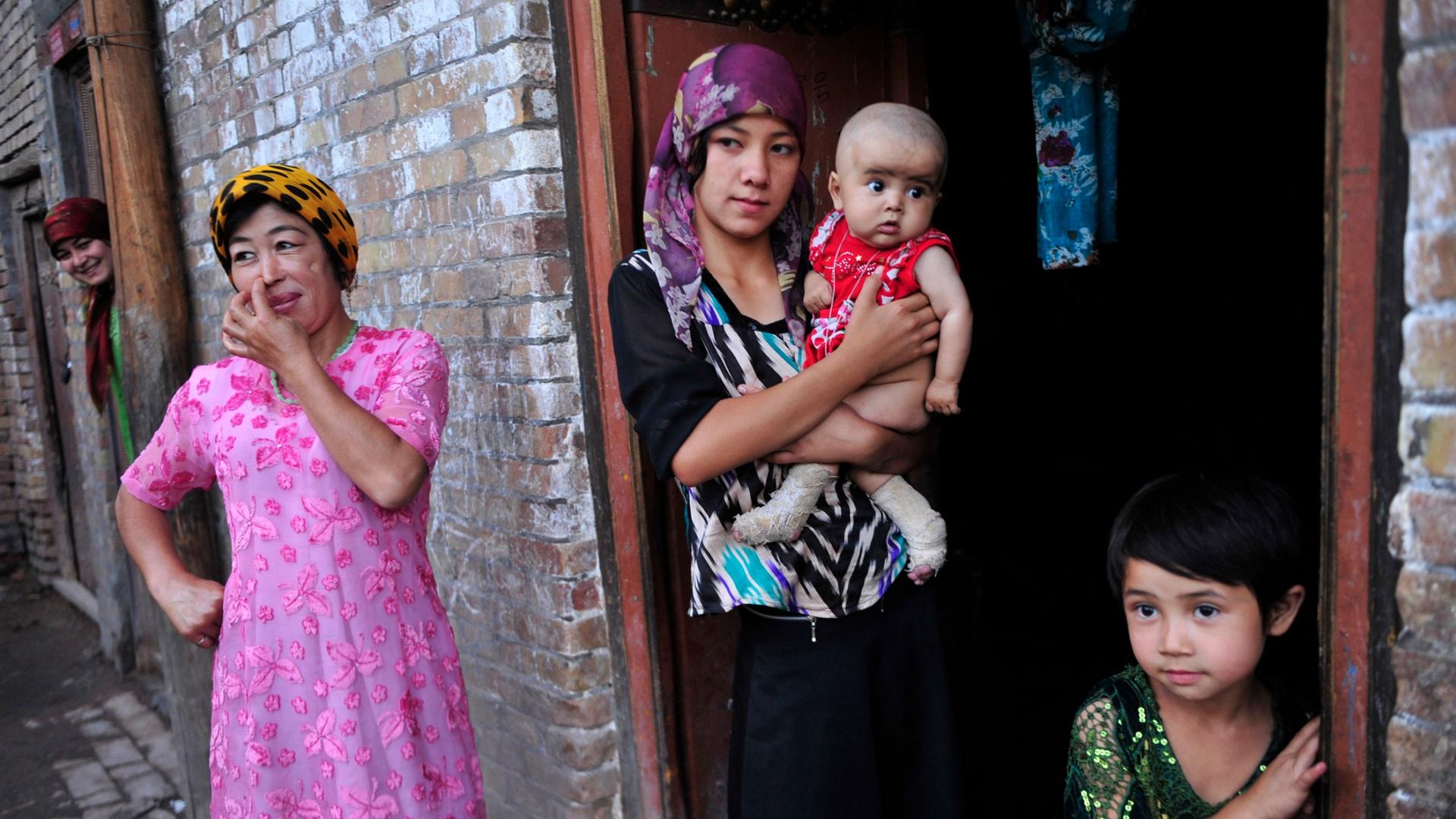 An ethnic Uighur woman hugs her son as she stands outside her house with her daughter and neighbors