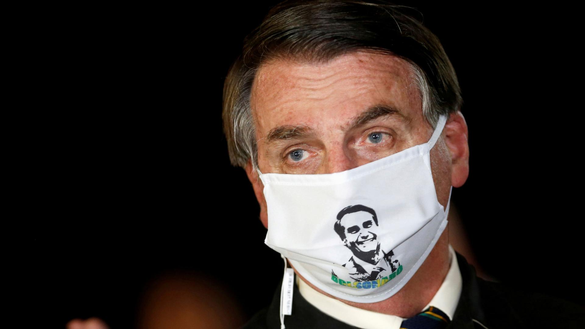 Brazil's President Jair Bolsonaro is shown wearing a white mask with his face printed on it.
