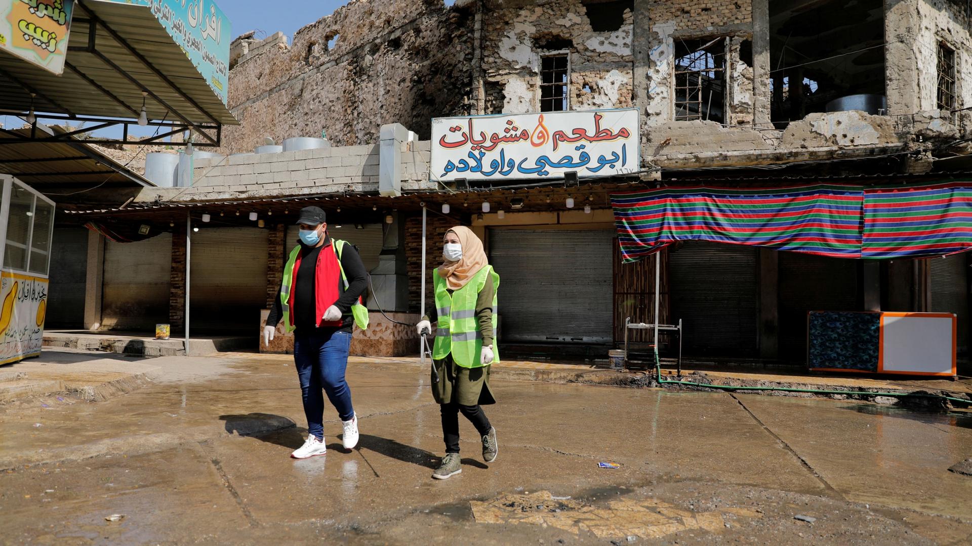 Two young people are shown walking in an empty courtyard and wearing safety vests and protective face masks.