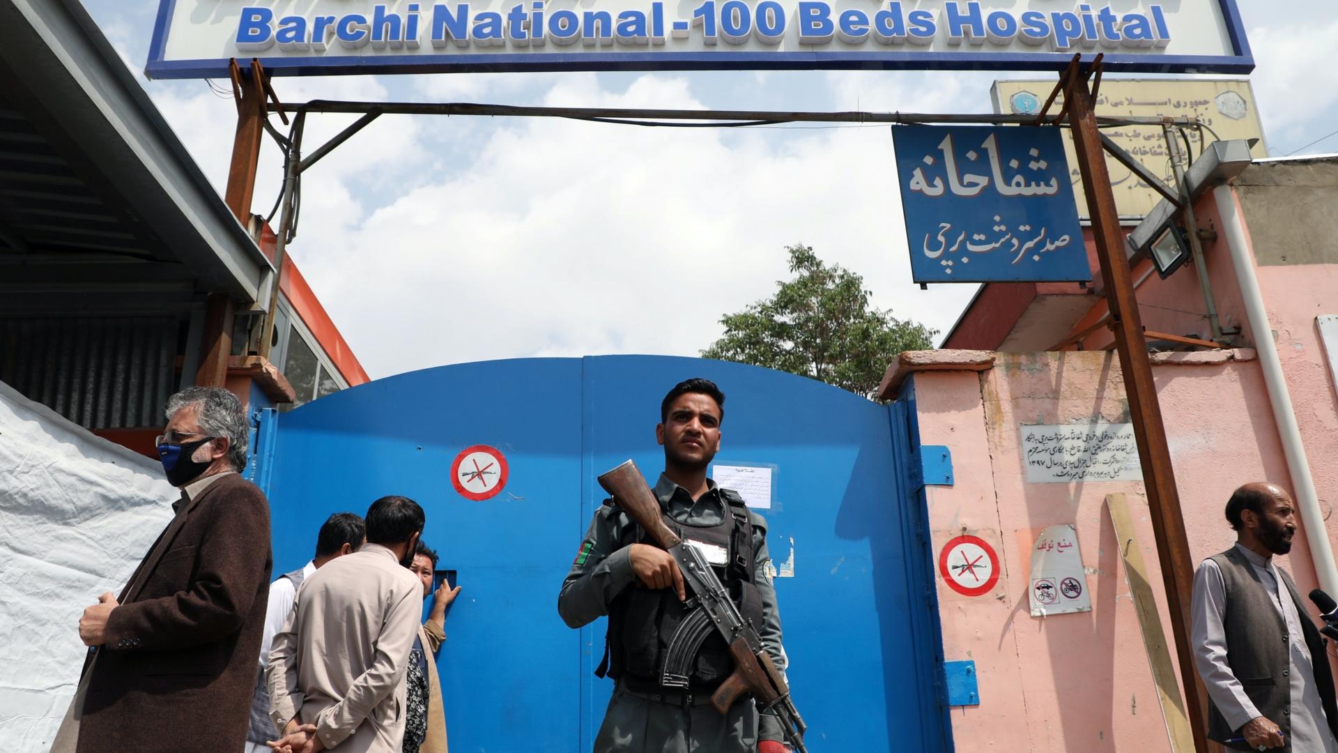 A man with a gun stands in front of a blue door of a hospital that got attacked. 