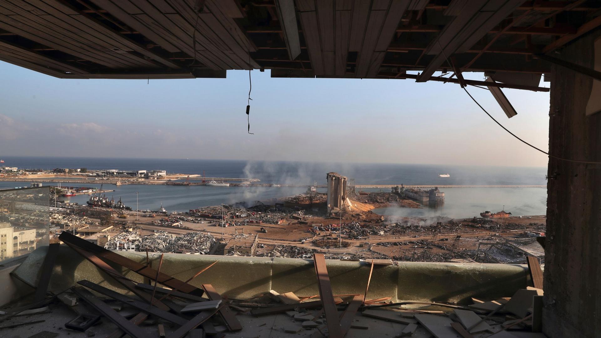 A view of the site of an explosion in the port of Beirut with buildings turned to rubble and shown from inside a facility with it's window blown out.