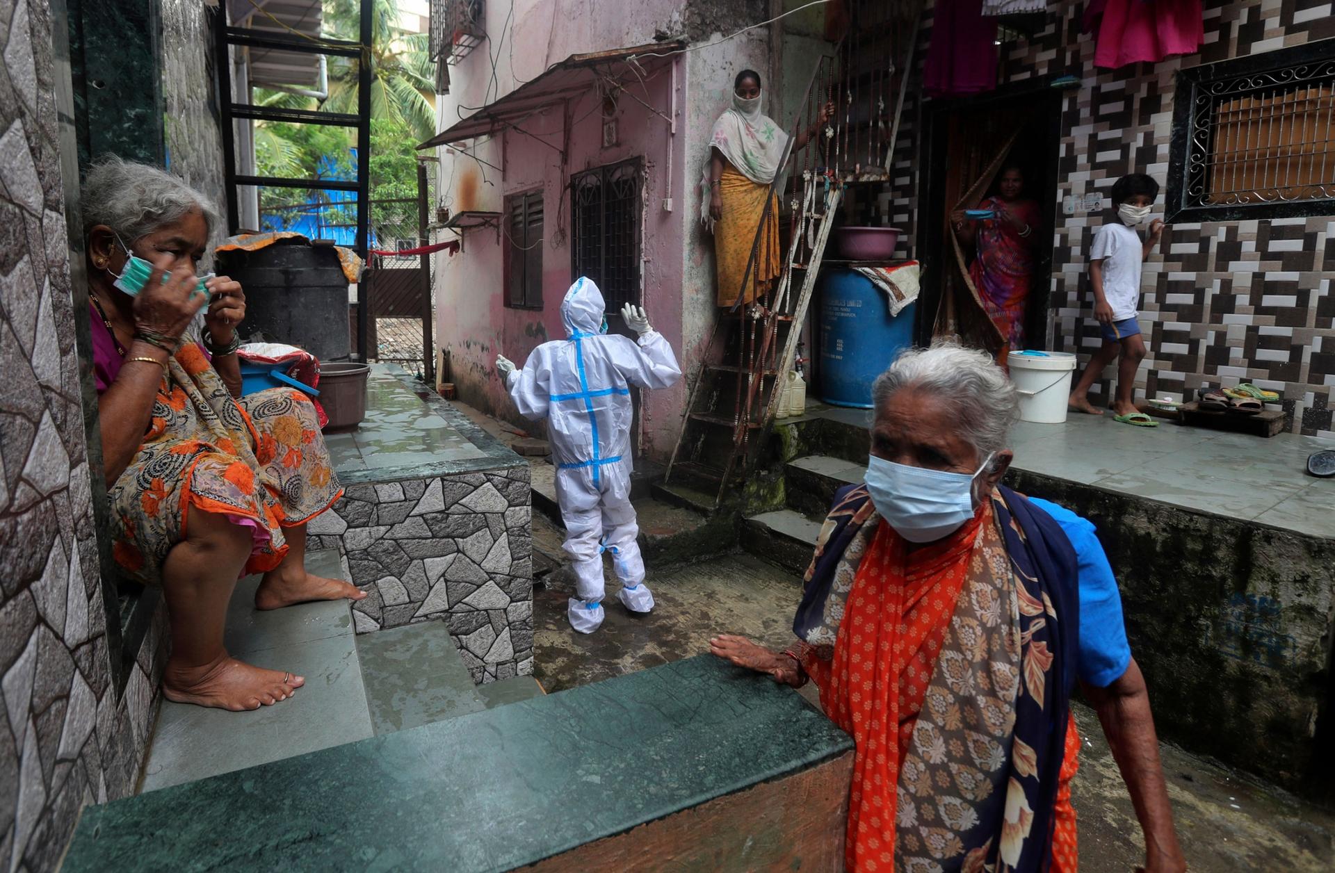 Several people are shown wearing brightly color saris with a peron center frame wearing a full protective medical outfit.