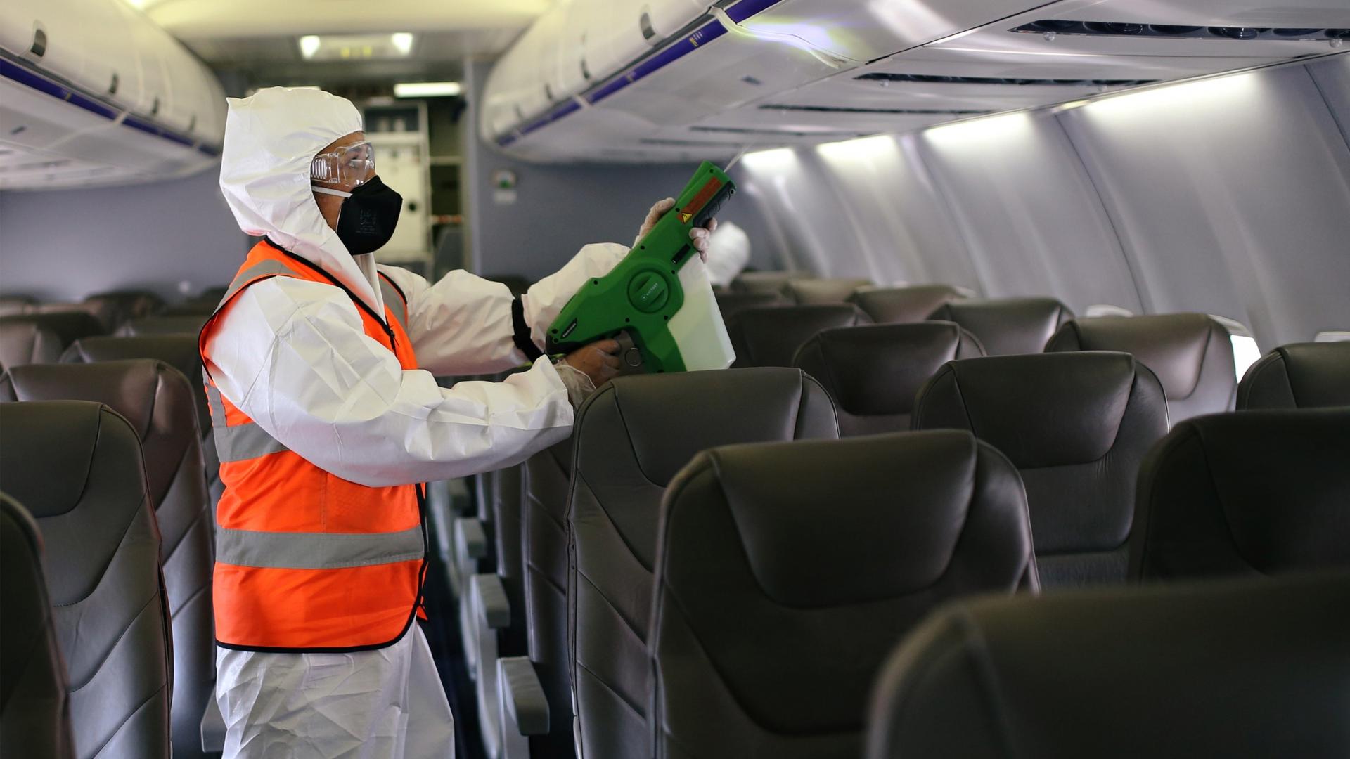 A person wearing a hazmat suit appears cleaning inside an airplane.