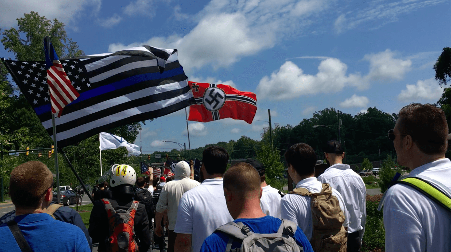 White men walk down a street with white power flags showing Nazi symbols 