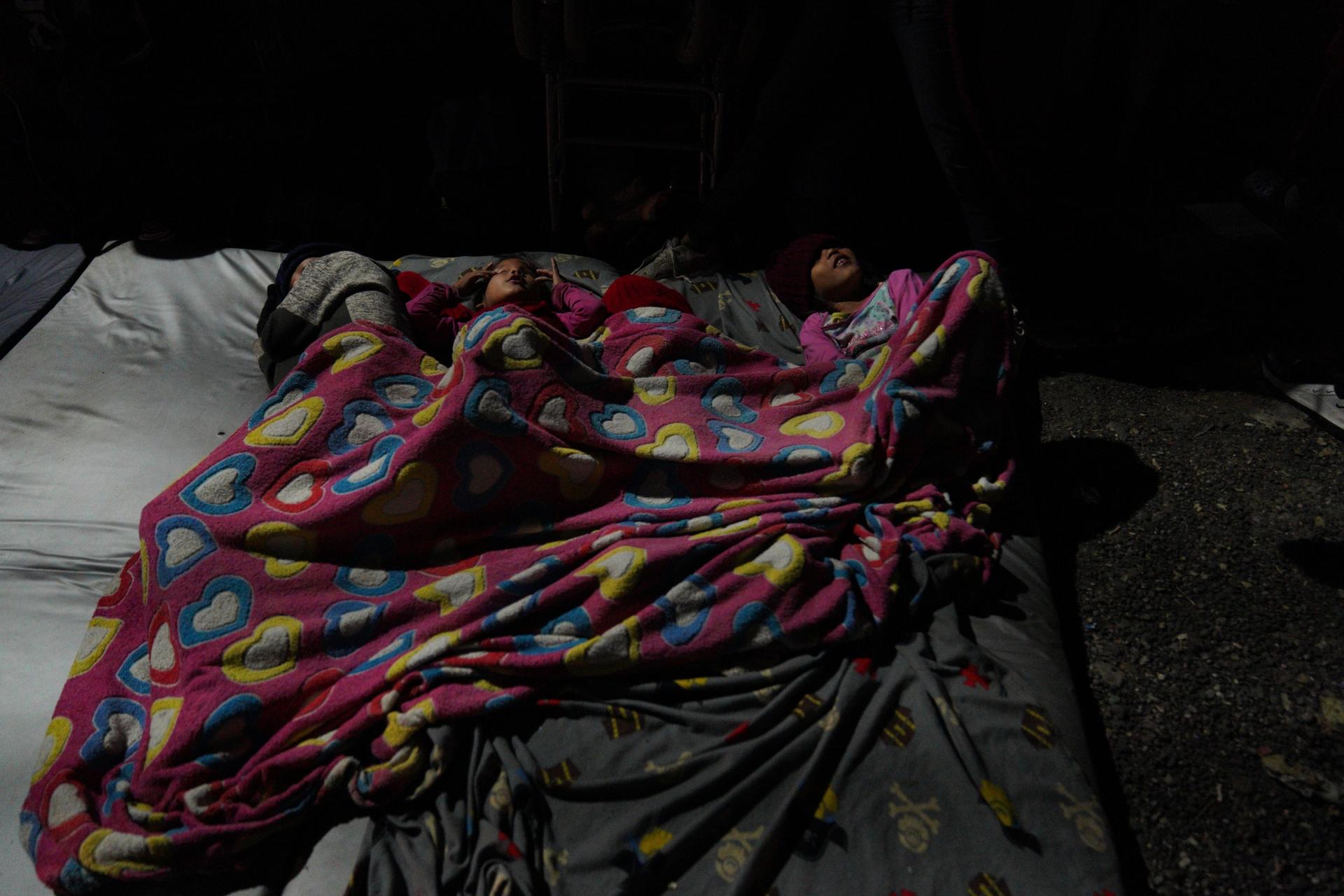 A family sleeps in a blanket on the street. 