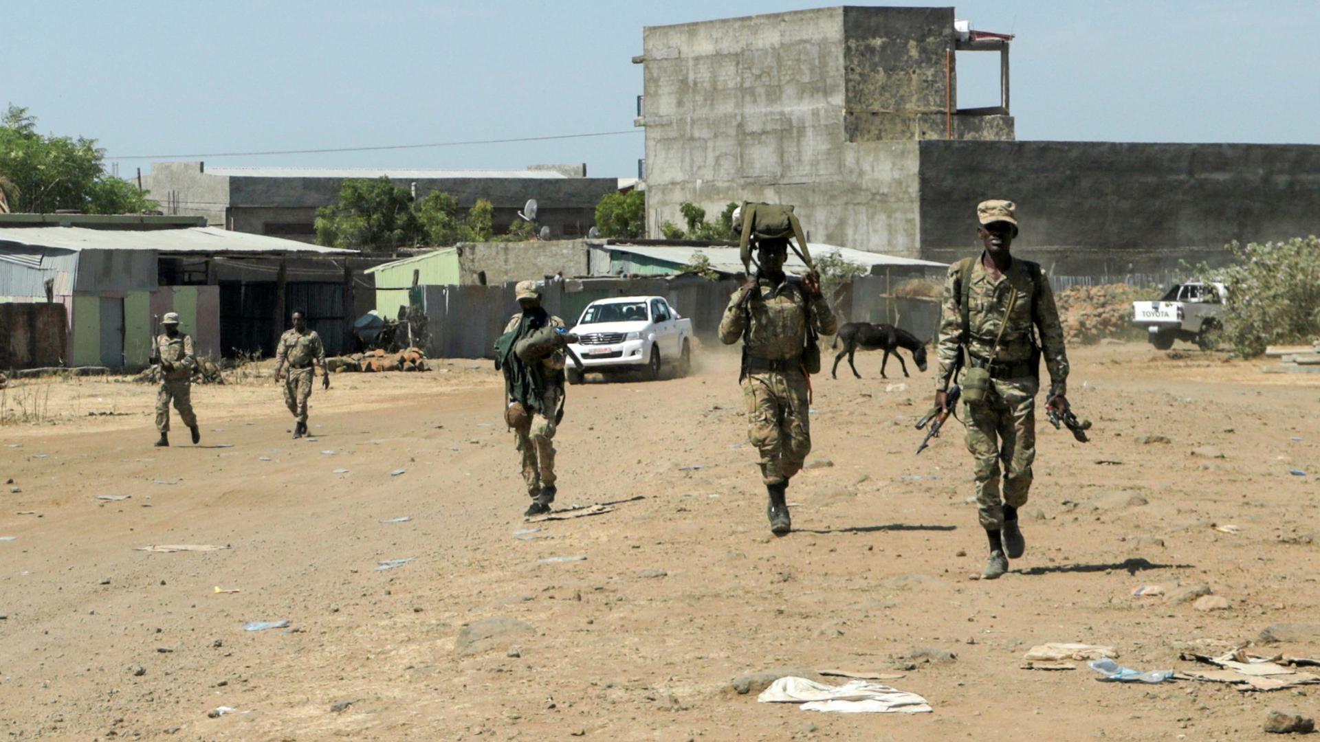 A small group of soldiers are shown walking and carrying weapons with a large cement structure in the distance.