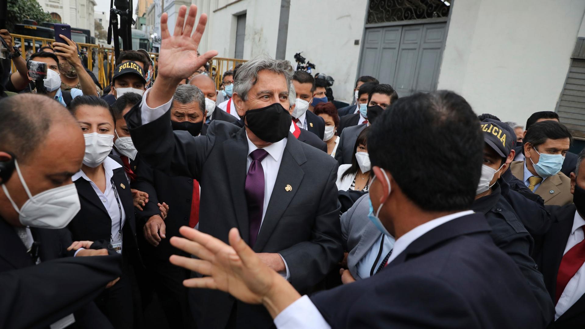 Peru's new President Francisco Sagasti is shown among a large crowd of people while wearing a face mask and waving.