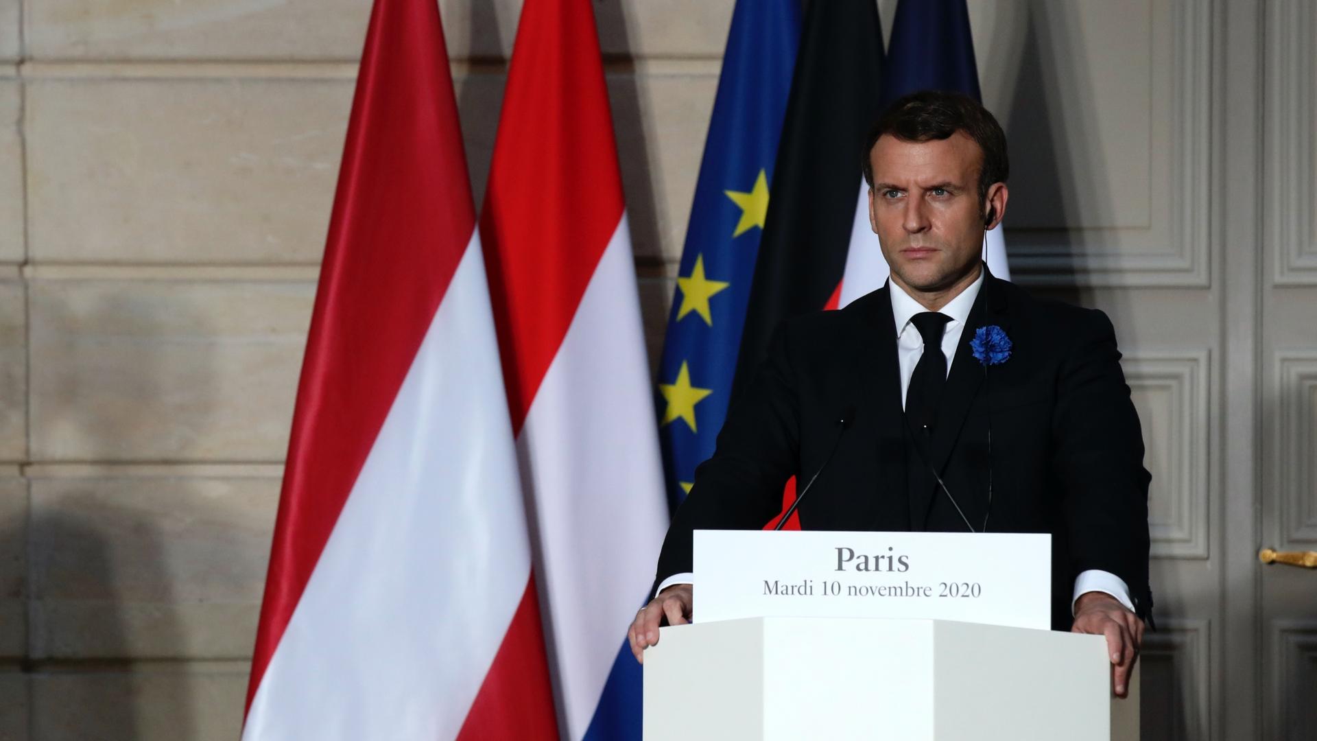 French President Emmanuel Macron stands at a podium with French flag behind him. 
