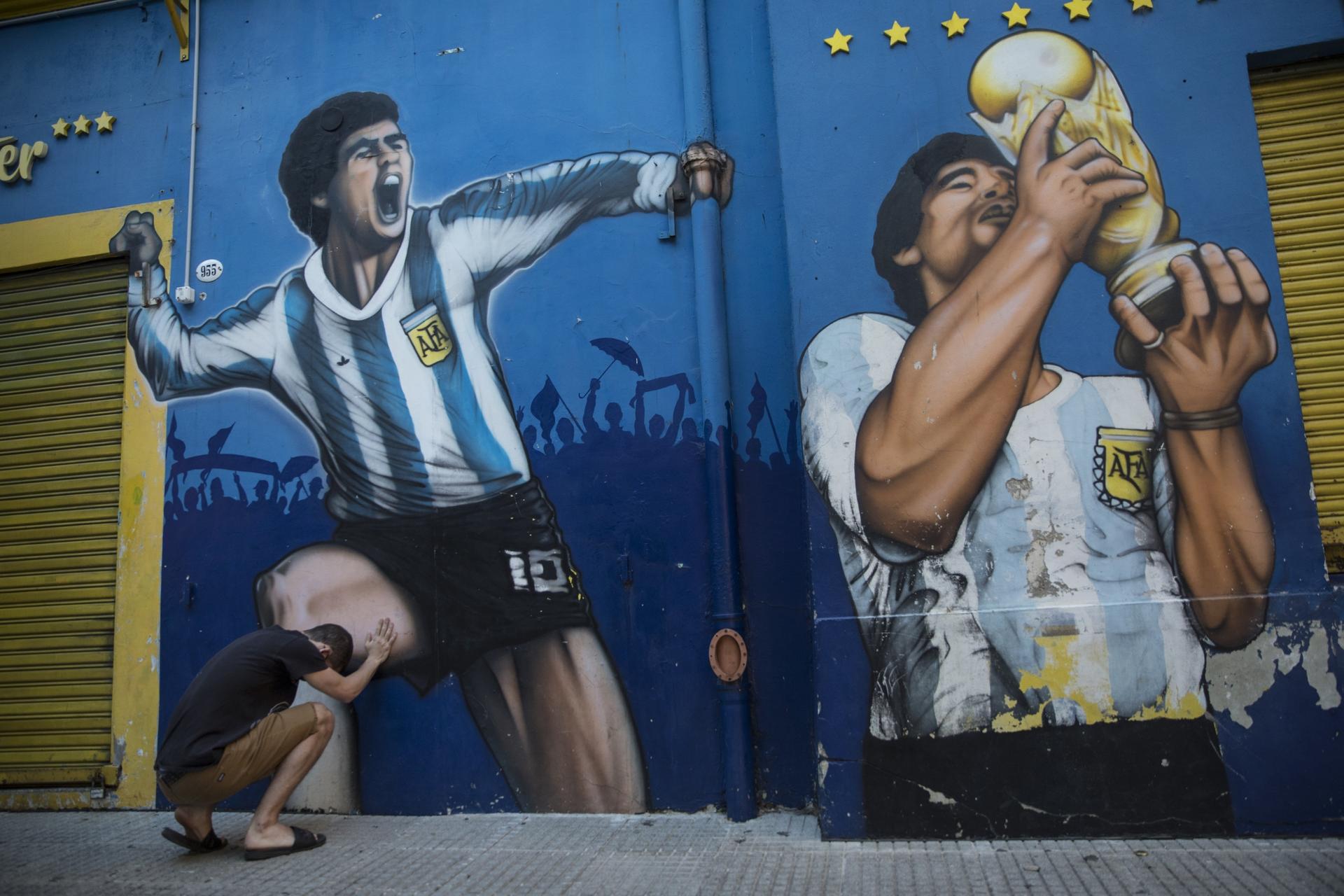 A man prays while touching a painting of Diego Maradona near the Boca Juniors stadium in Buenos Aires, Argentina, Nov. 27, 2020. 