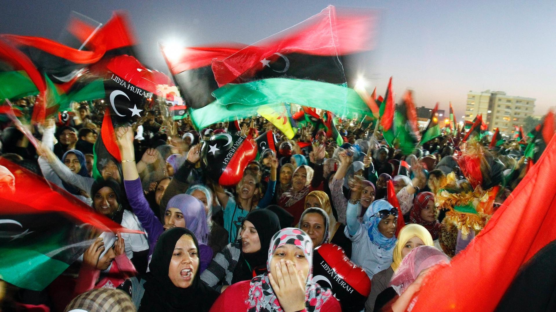 A crowd of people celebrate with flashes of red, black and green flags waving in the air. 