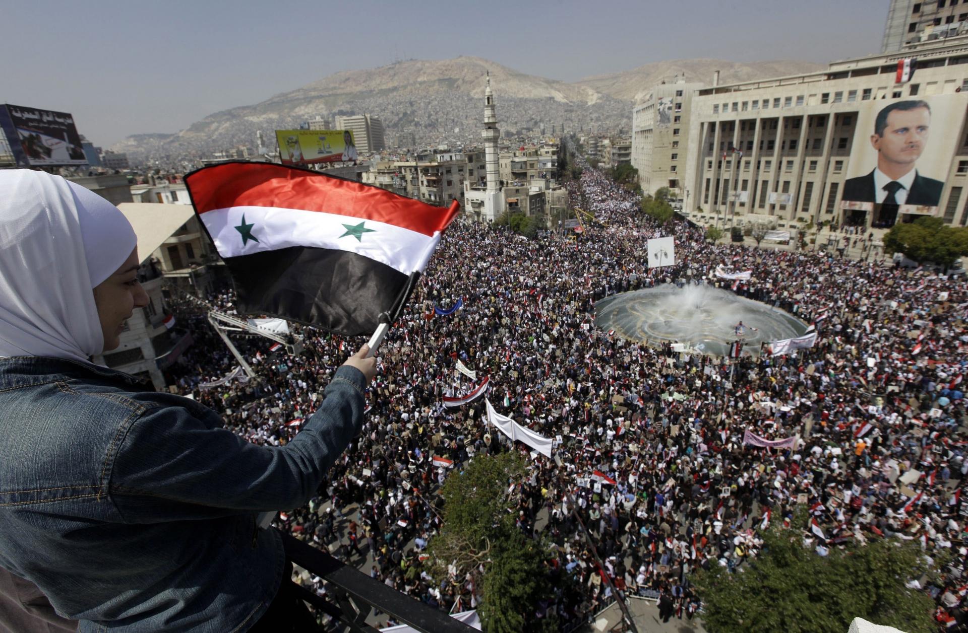 A supporter of Syrian President Bashar Assad waves a Syrian flag as she looks over a crowd gathered to show support for their president in Damascus, Syria, March 29, 2011.