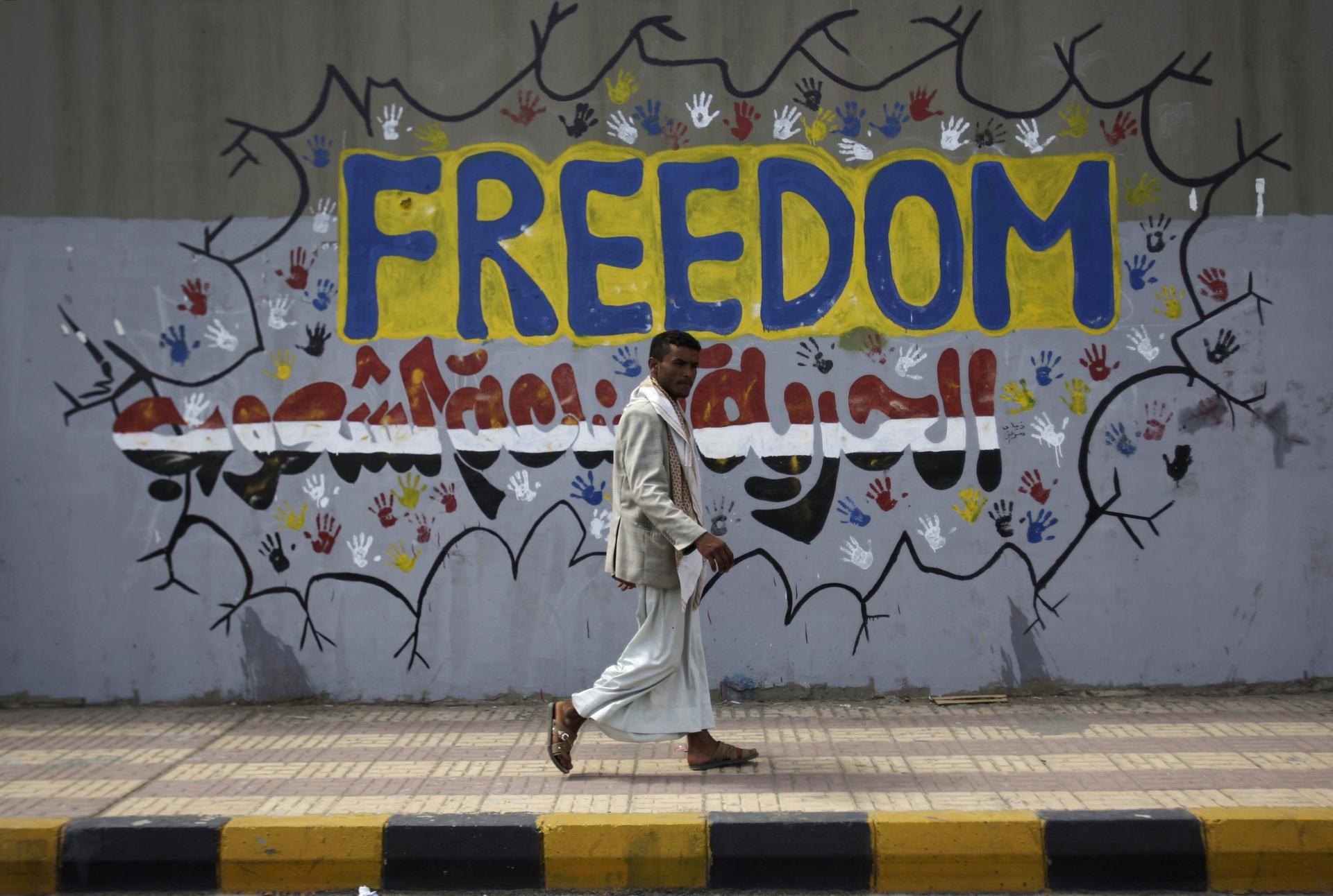 In this Friday, March 2, 2012 file photo, a Yemeni walks past a graffiti that reads "Freedom is made by people" on a street where protesters demanded a trial for the former President Ali Abdullah Saleh, in Sanaa, Yemen.