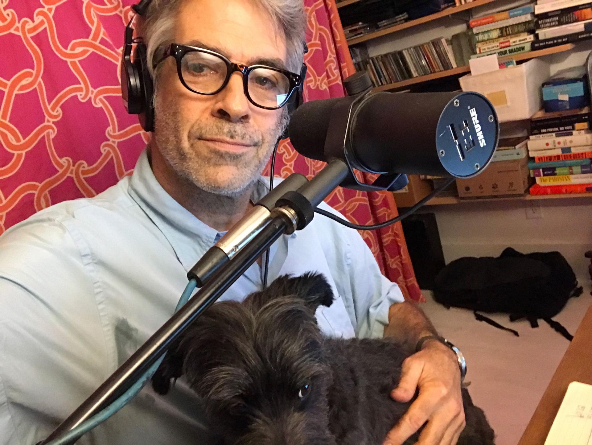 Marco Werman is shown with a microphone and his dog Frankie sitting on his lap.