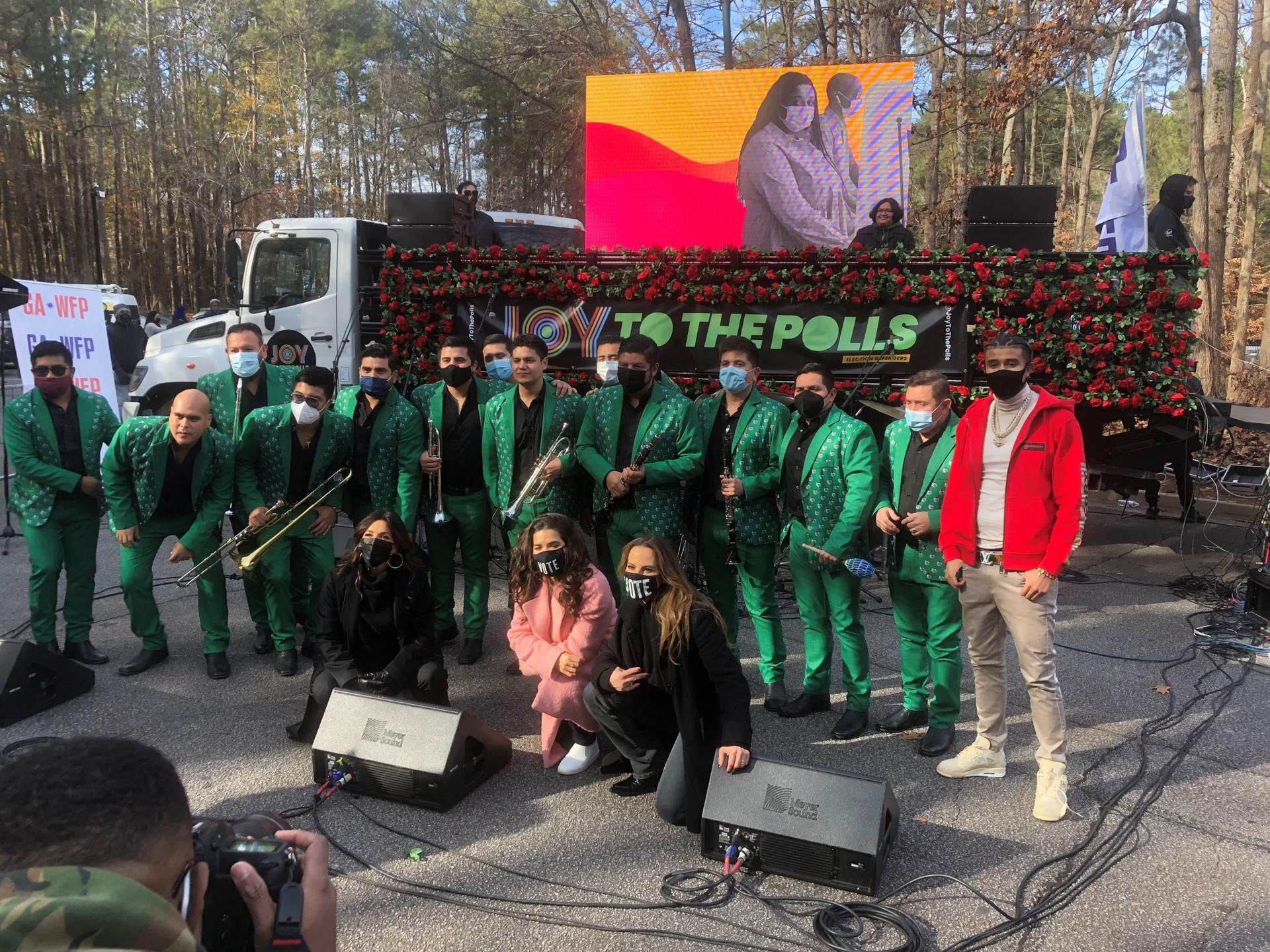 A group of musicians wearing green uniforms and other actors and musicians stand outside together. 