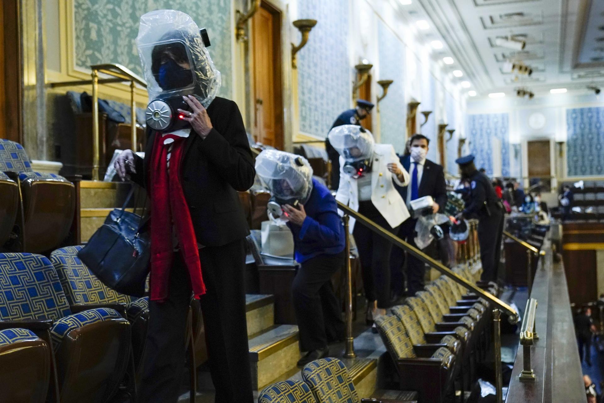People wearing plastic protection around their heads shelter in the House gallery as a mob of Trump supporters try to break into the House chamber at the US Capitol on Wednesday, Jan. 6, 2021, in Washington, DC.