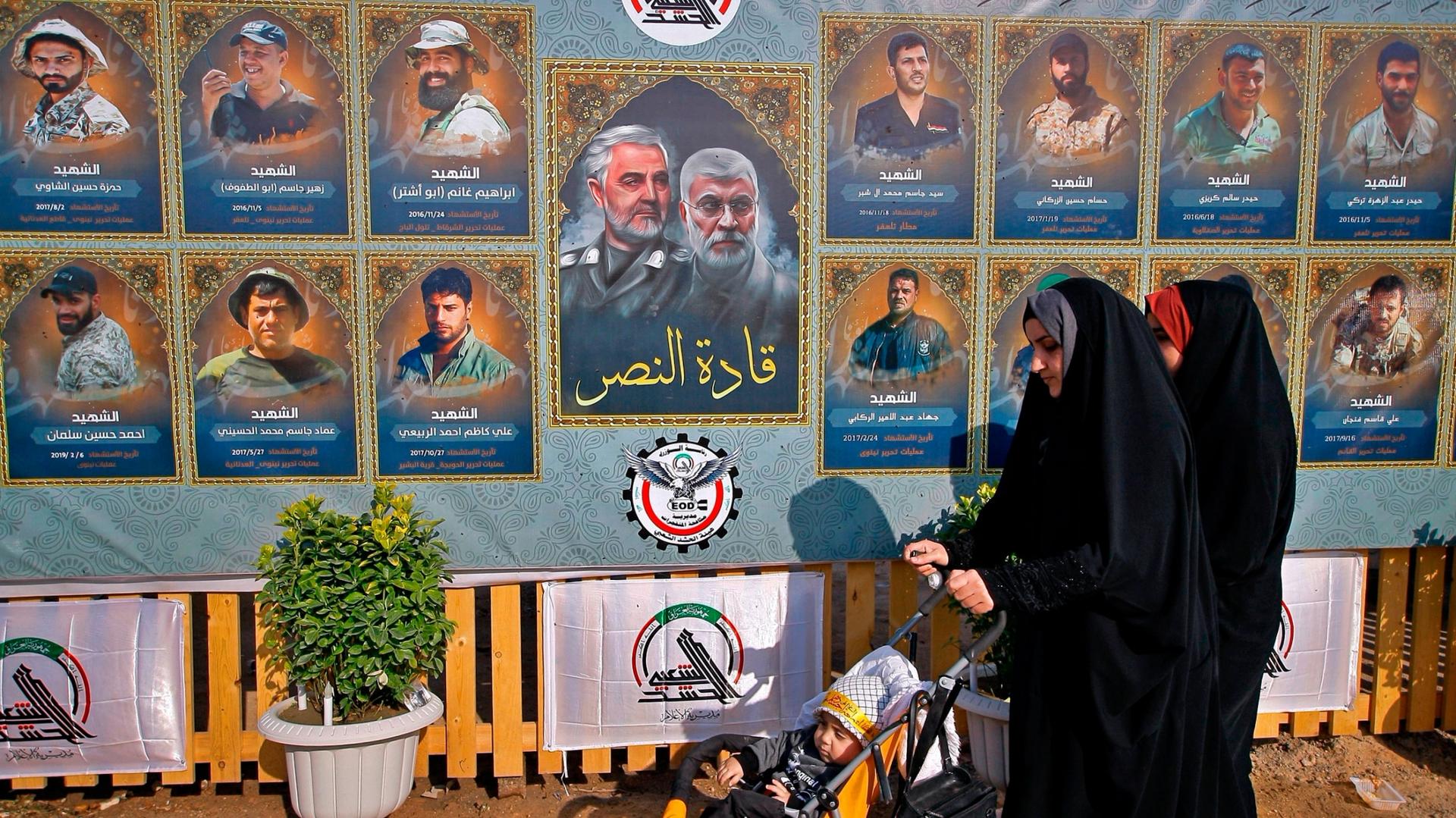 People pass by posters of Gen. Qassem Soleimani along with several other illustrated portraits alongside. 