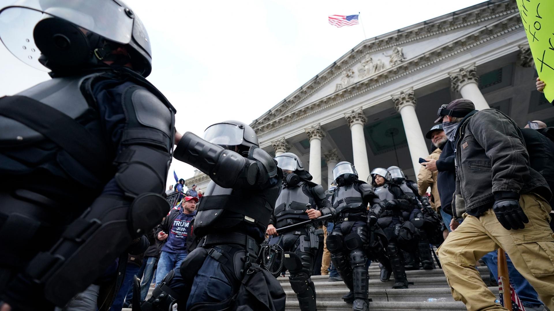 A line of police are shown walking down the Capitol building staircase dressed in black armor with helmets.