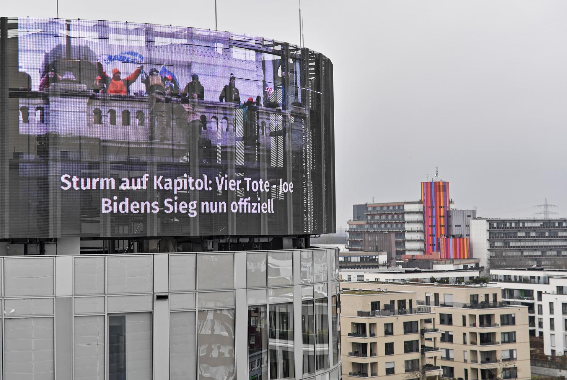 A big news screen on a building in Essen, Germany, showing protesters on the US Capitol in Washington, a headline reads "Storm on the Capitol: Four dead — Joe Biden's victory now official," on Thursday, Jan. 7, 2021. 