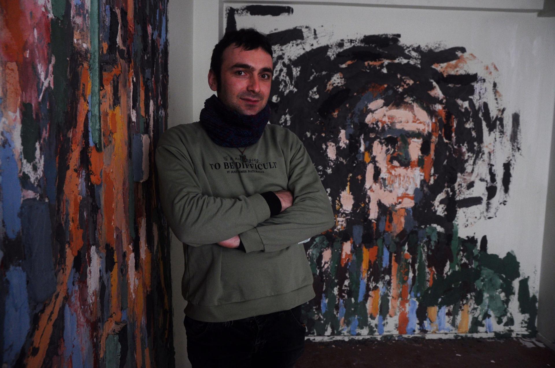Batikan Bostanci, 30, stands with his installation, “Powerless Faces.” Bostanci layered pigments and paint over textured concrete, wood and plastic remnants found in the debris left by the building’s residents. 