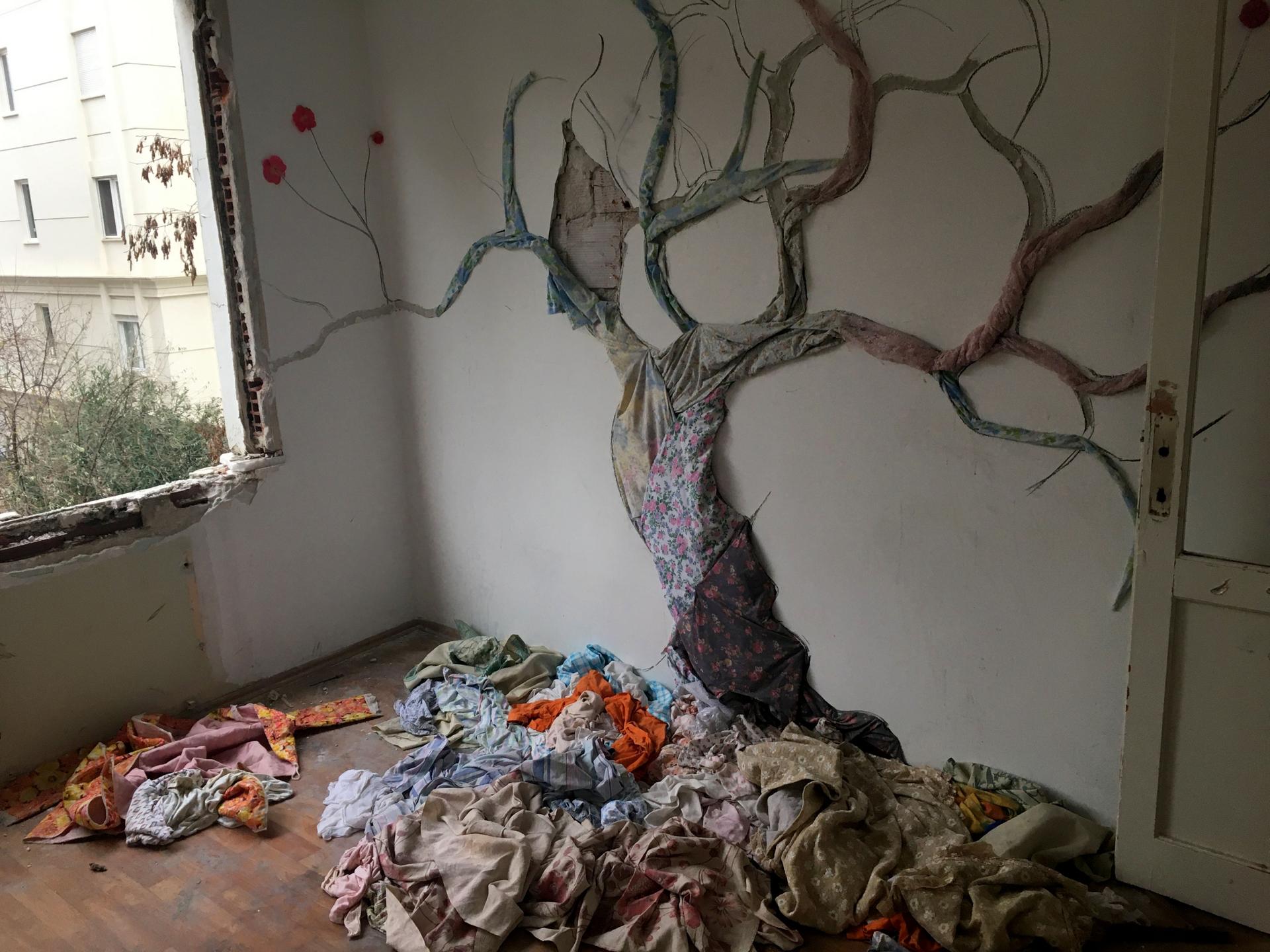 A tree made of found fabrics pinned to a wall by Songul Girgin gazes wistfully out of what was once a bedroom window. 