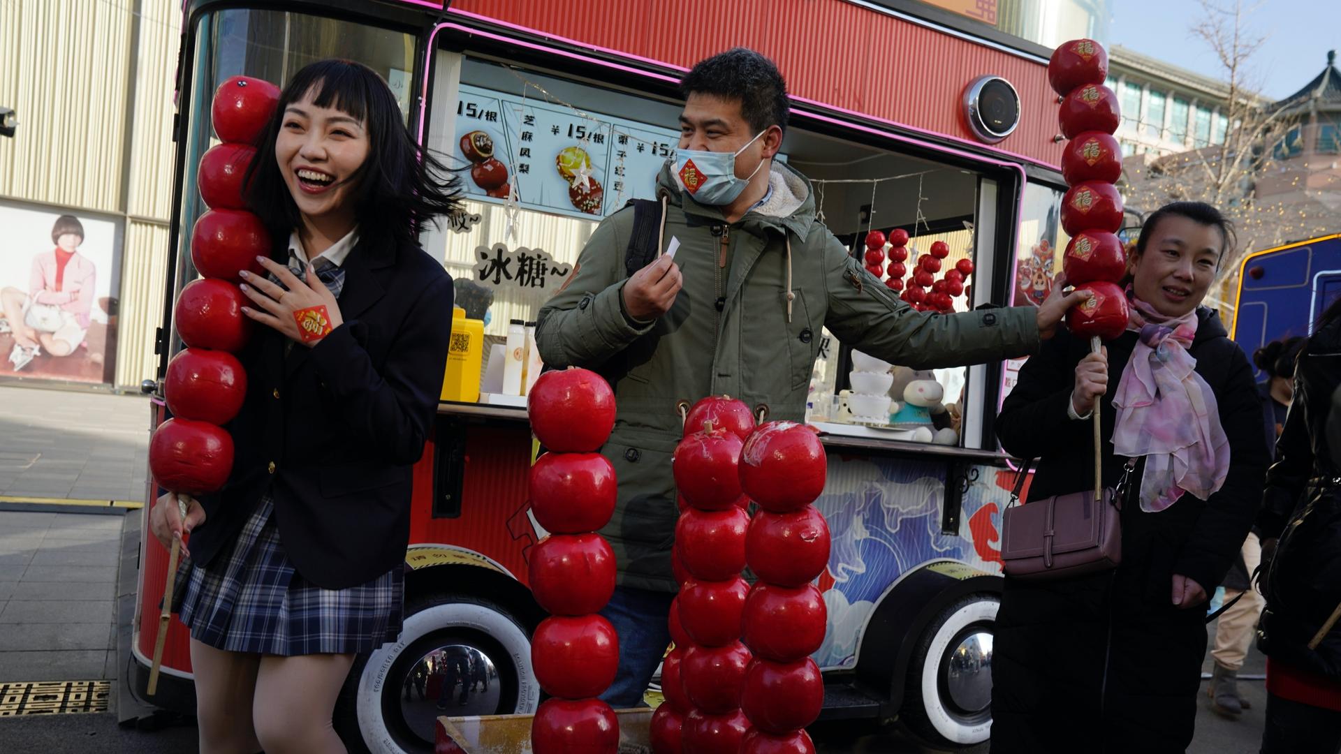 A Chinese woman reacts as she holds a giant replica of candy haw, a popular Beijing snack, at a street stall near Wangfujing on the fourth day of the Lunar Chinese New Year in Beijing on Feb. 15, 2021.