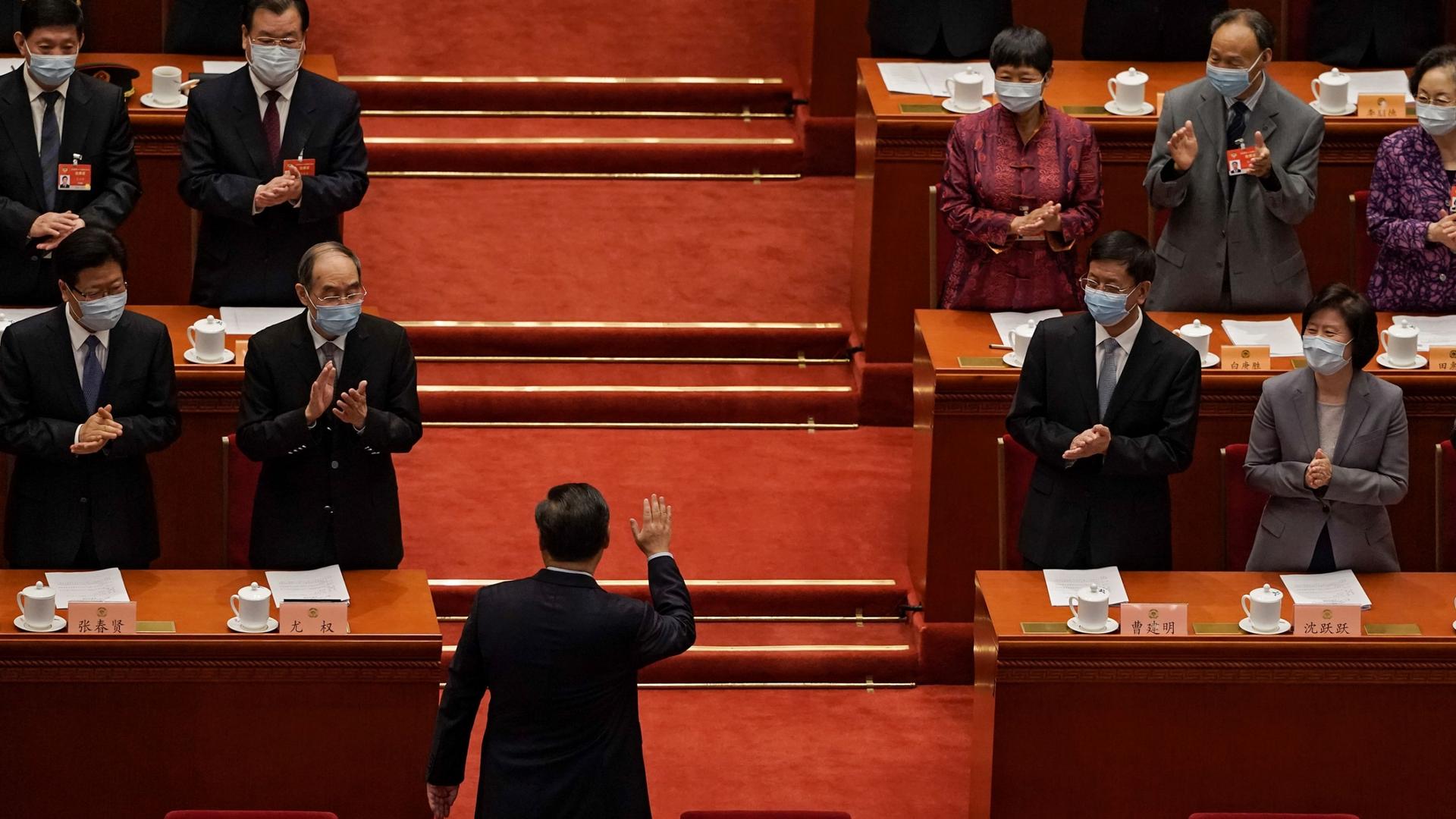 Chinese President Xi Jinping is shown with his back toward the camera and facing several rows of government officials who are clapping.