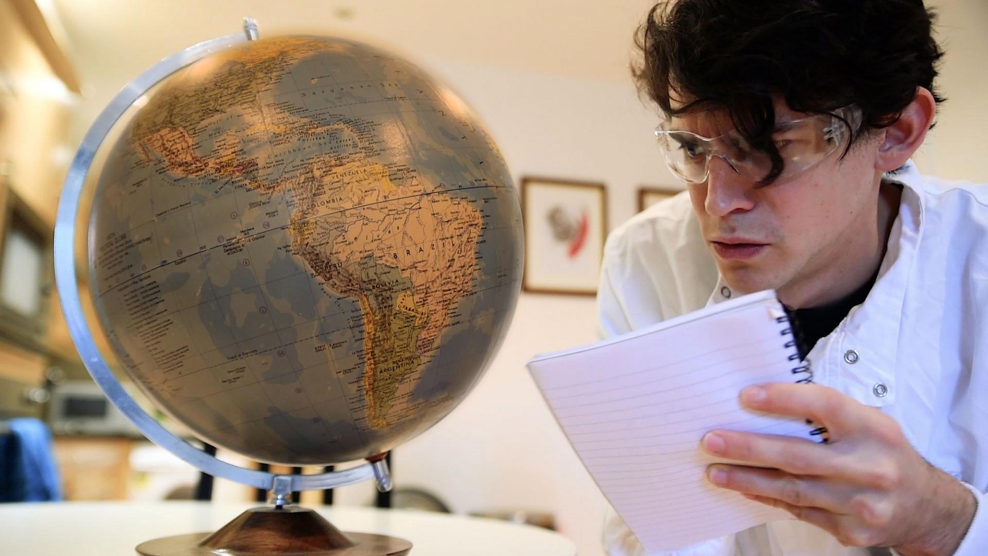 A man wearing glasses looks at a globe. 